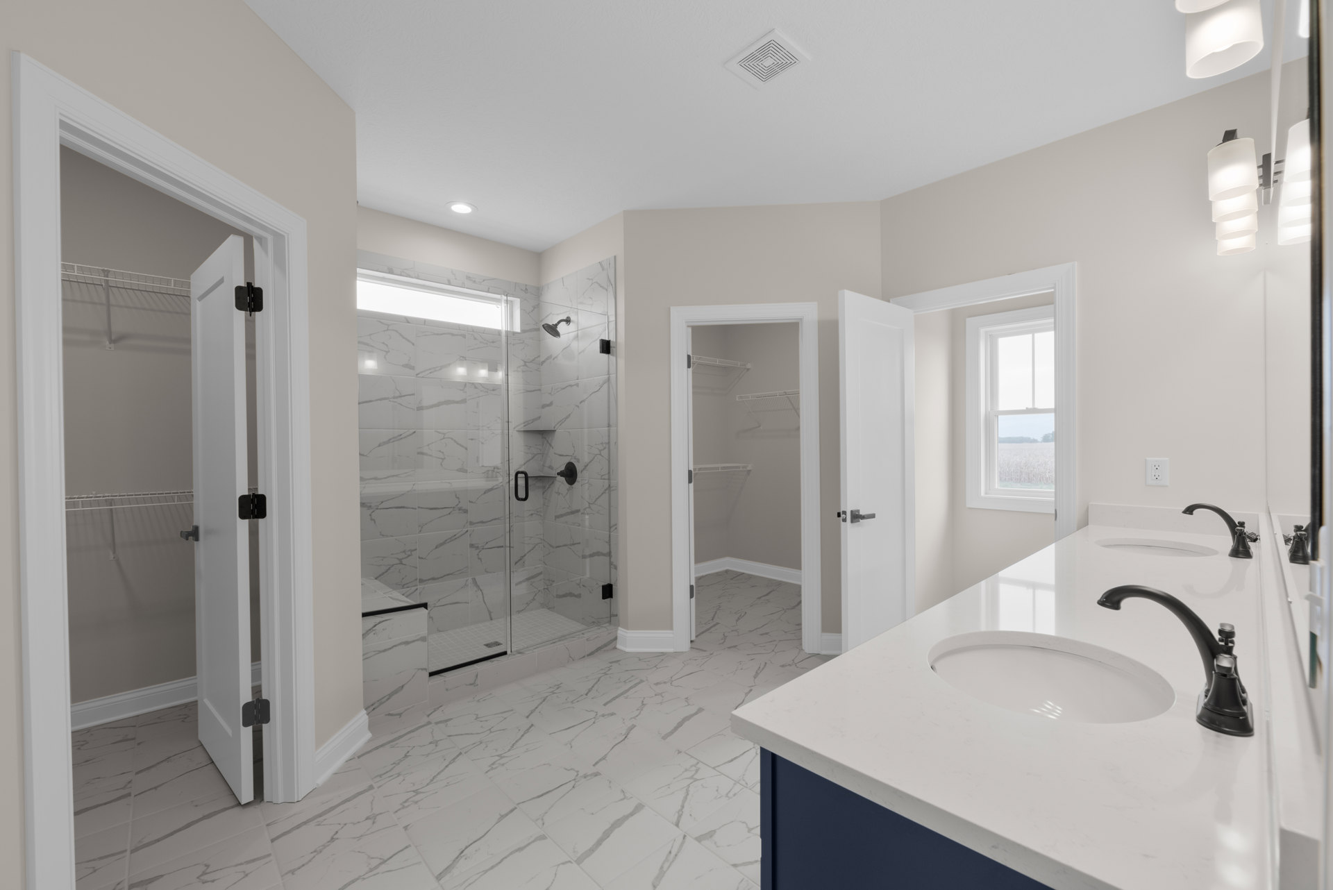 Bathroom with marble tile floor, glass-enclosed shower, white sink with chrome faucet, and modern light fixture