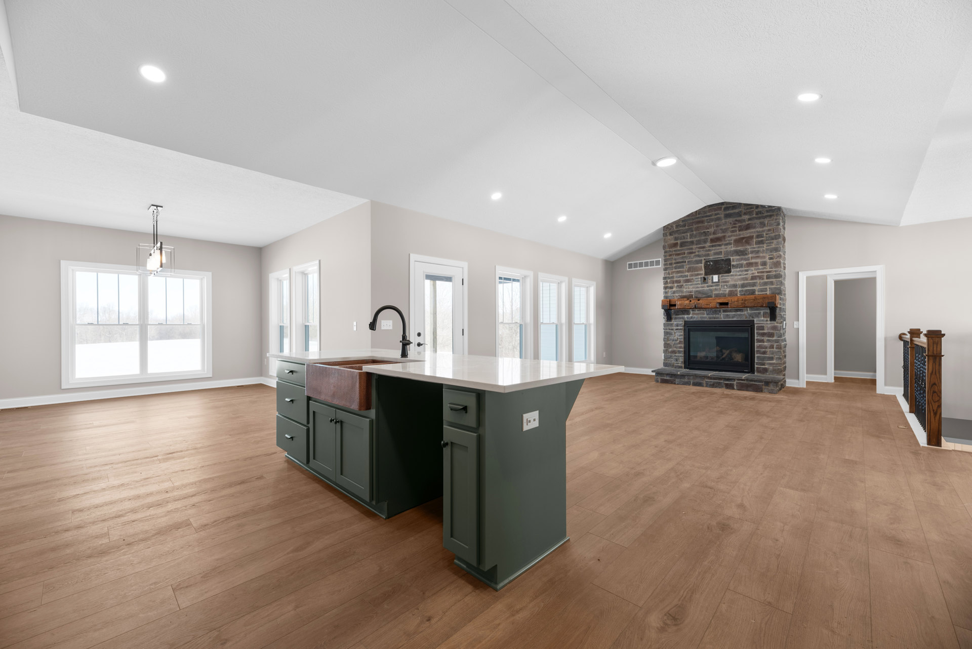 Spacious open-plan living area featuring a glass-door fireplace with wood mantel, kitchen island with sink, modern cabinetry, laminate flooring, and decorative light fixture