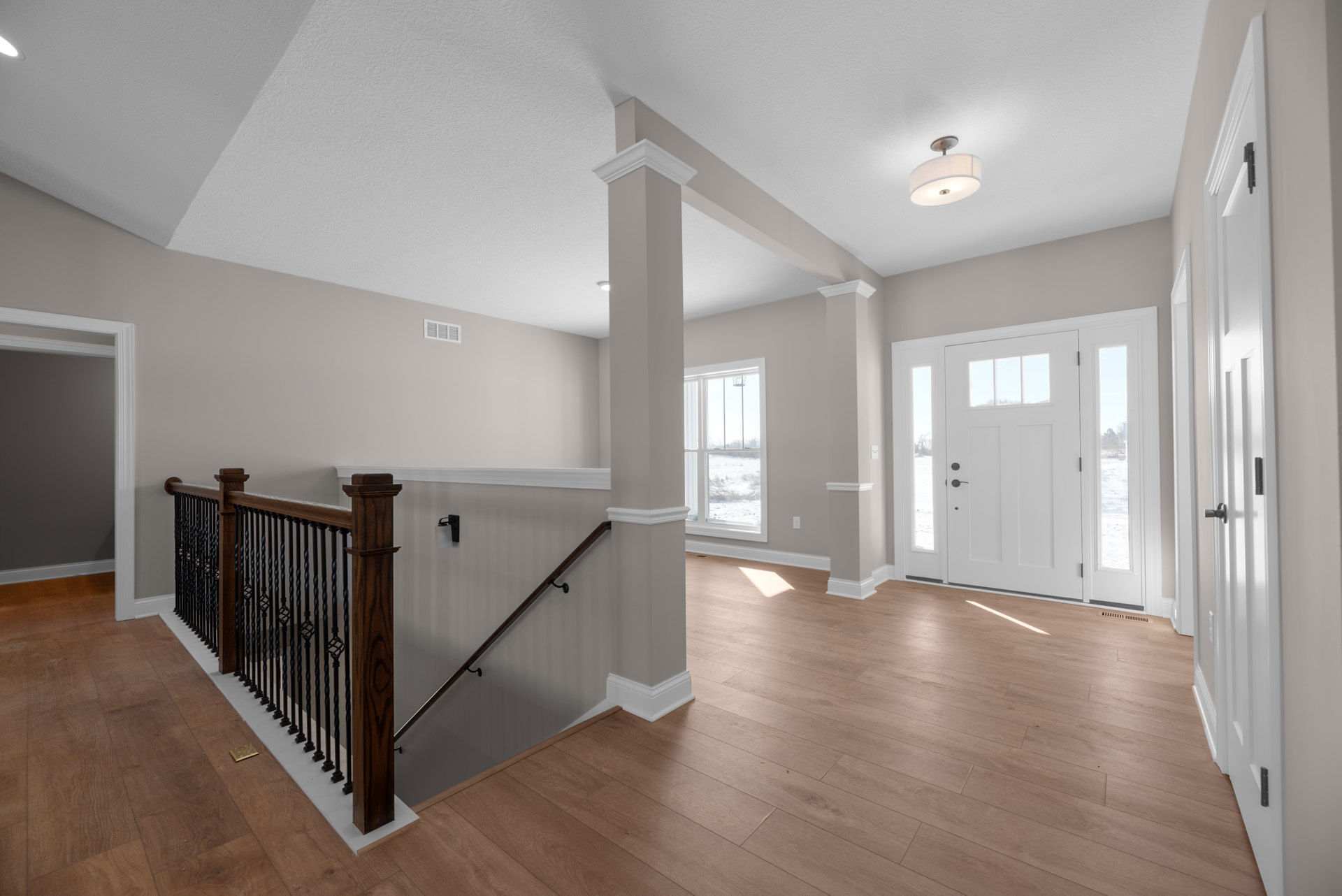 Hallway with wood flooring, white plaster walls, staircase featuring dark wood railing, white paneled door with glass inserts, and ceiling-mounted light fixture with white shade