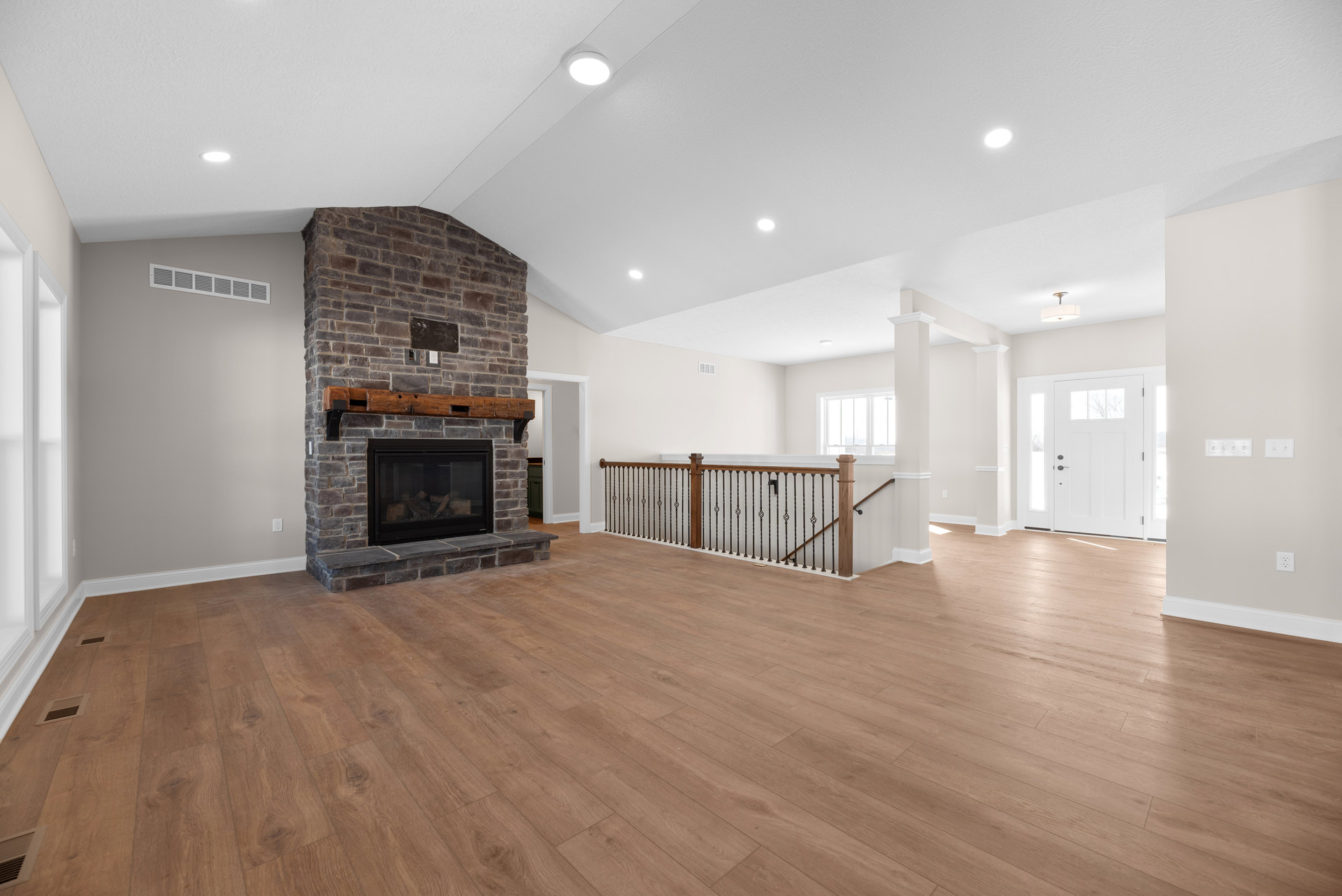Living room with hardwood flooring, stone fireplace with stacked wood, white door with glass panes, metal railing, and ceiling light fixture.