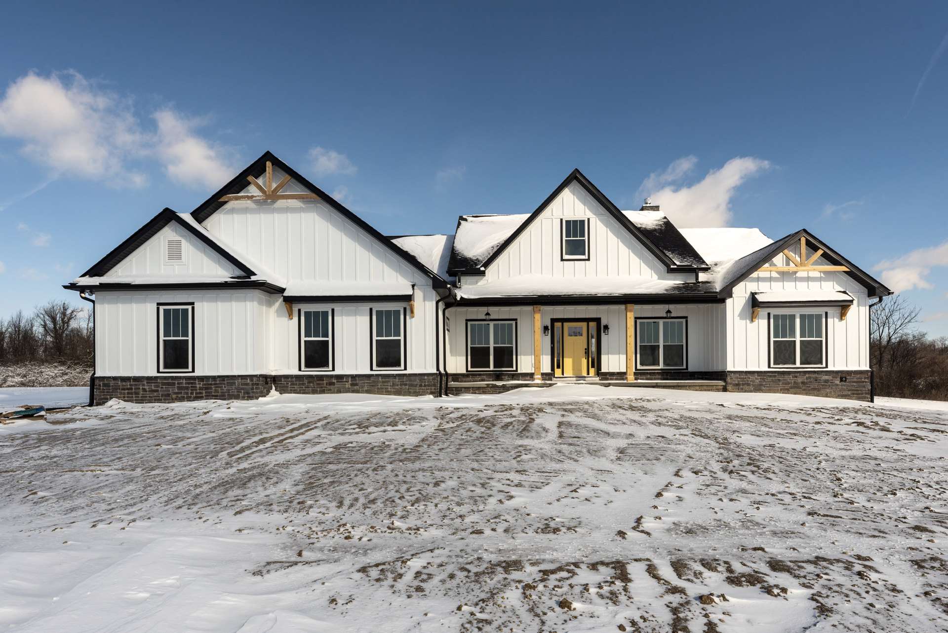 Yellow house with snow-covered roof and ground, double glass-paneled doors, large windows, and winter landscape.