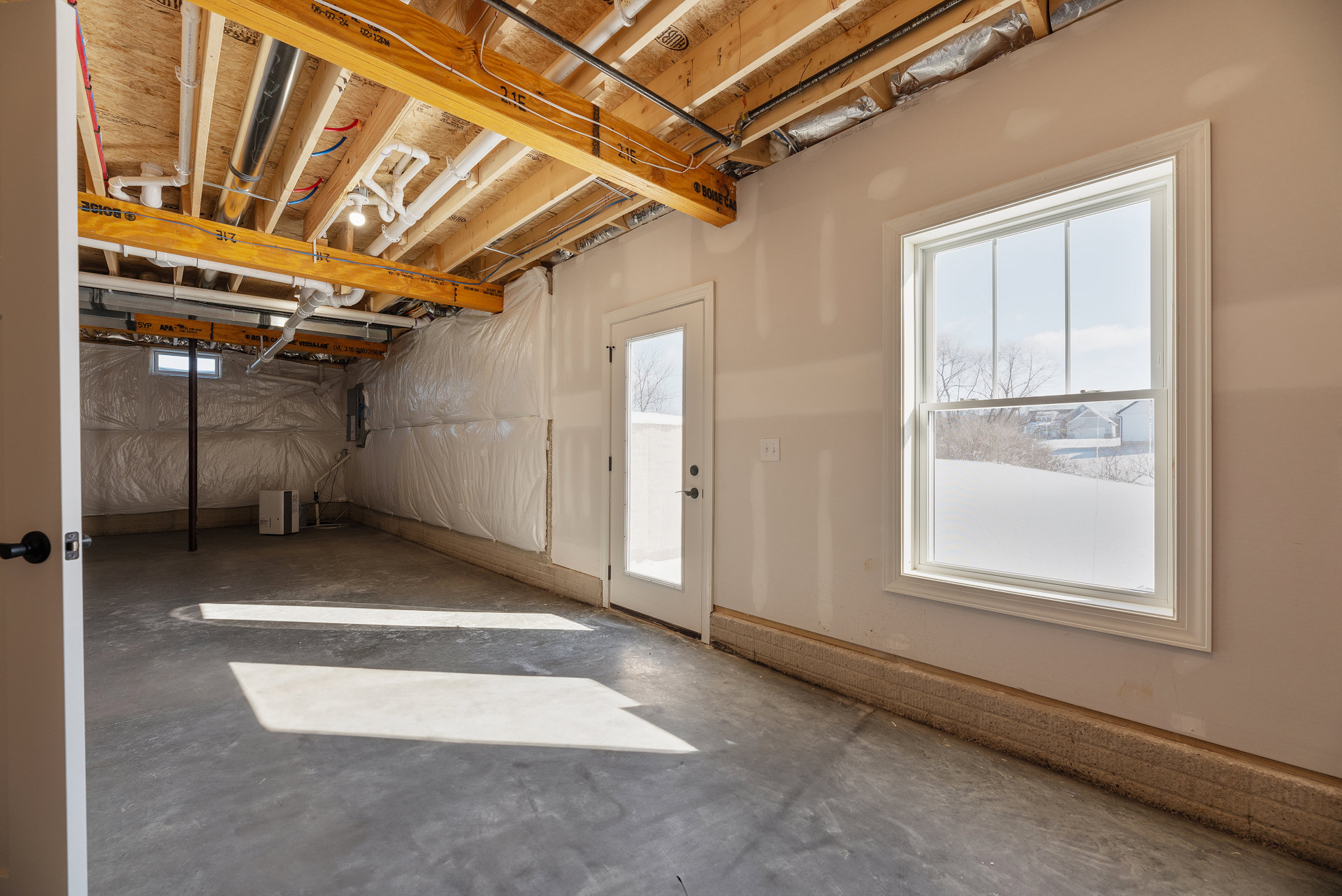 Bright room with white plaster walls, large windows overlooking snowy field, glass-paneled door, exposed beams, and daylight streaming in.