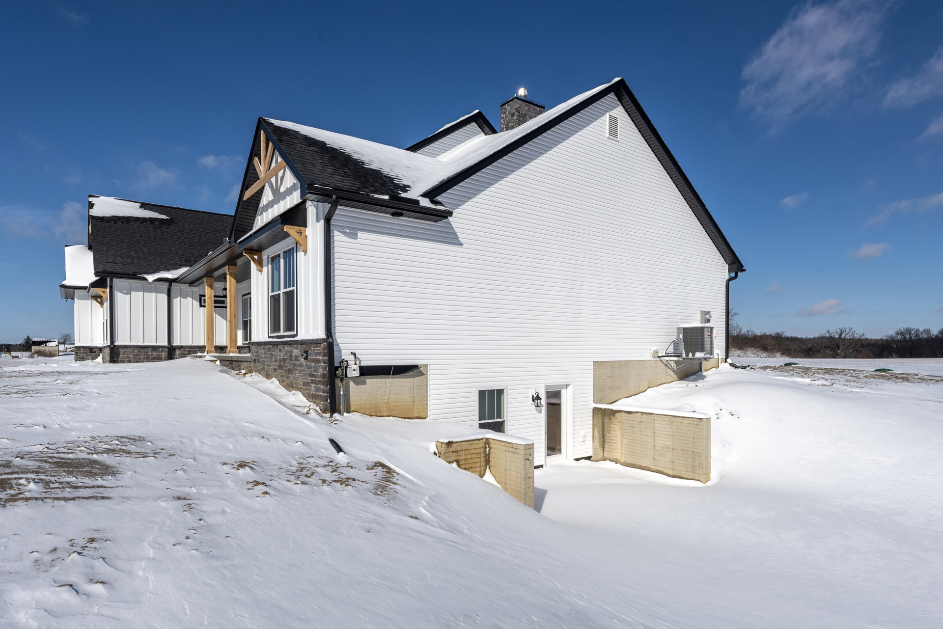 Two-story brick house with white-framed windows, snow covering the roof and ground, chimney topped with a light, winter sky overhead