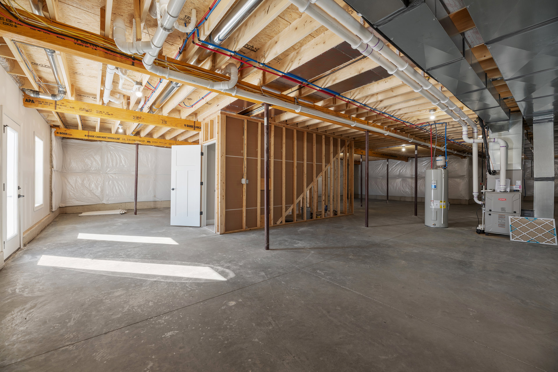 Utility room with exposed metal pipes, white cylindrical water filter labeled on side, insulated walls, white door with silver handle, unfinished ceiling beams