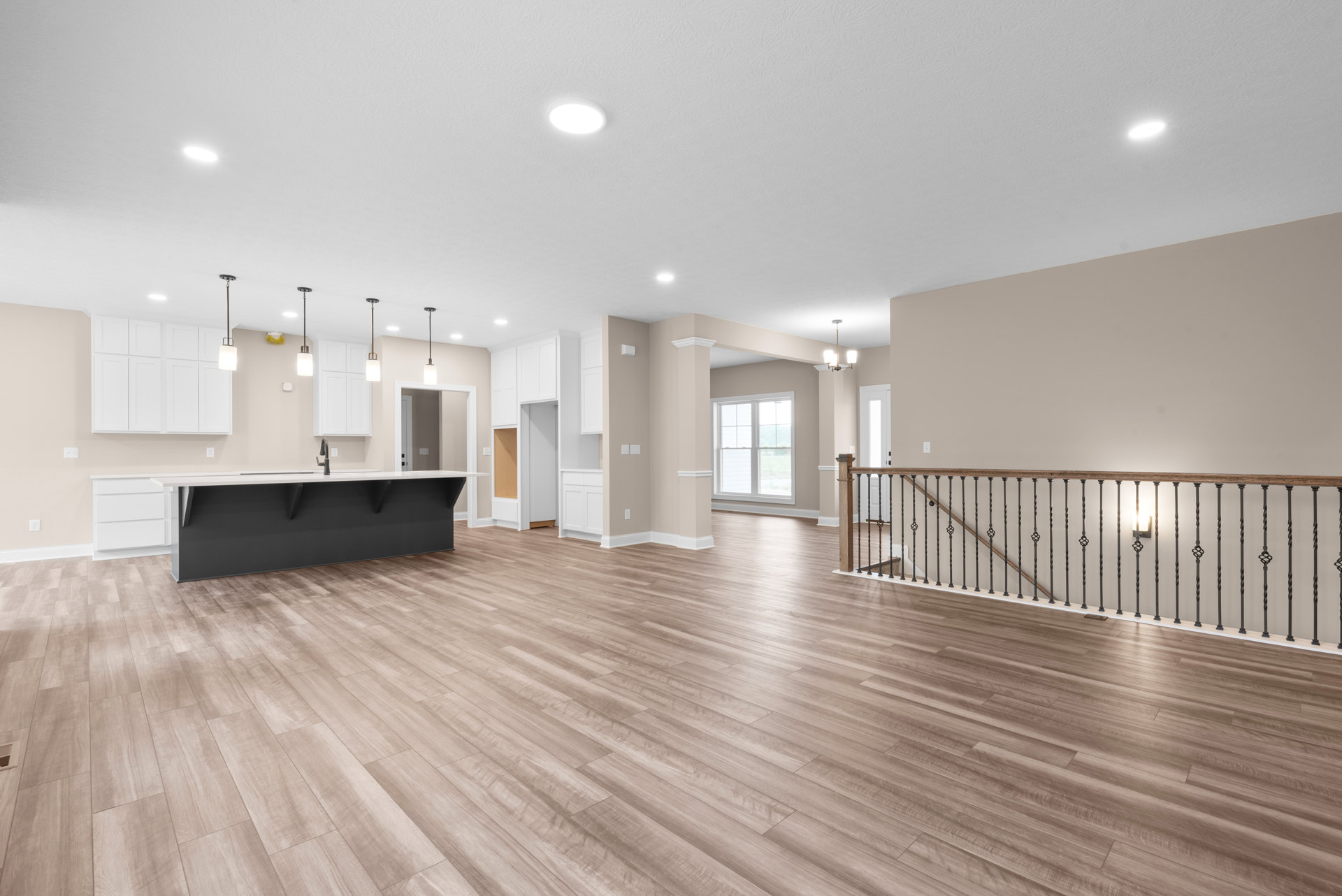 Open-plan room with hardwood flooring, white plaster walls, modern kitchen featuring a sink on a stone countertop, metal railing detail, ceiling light fixture, and large window.