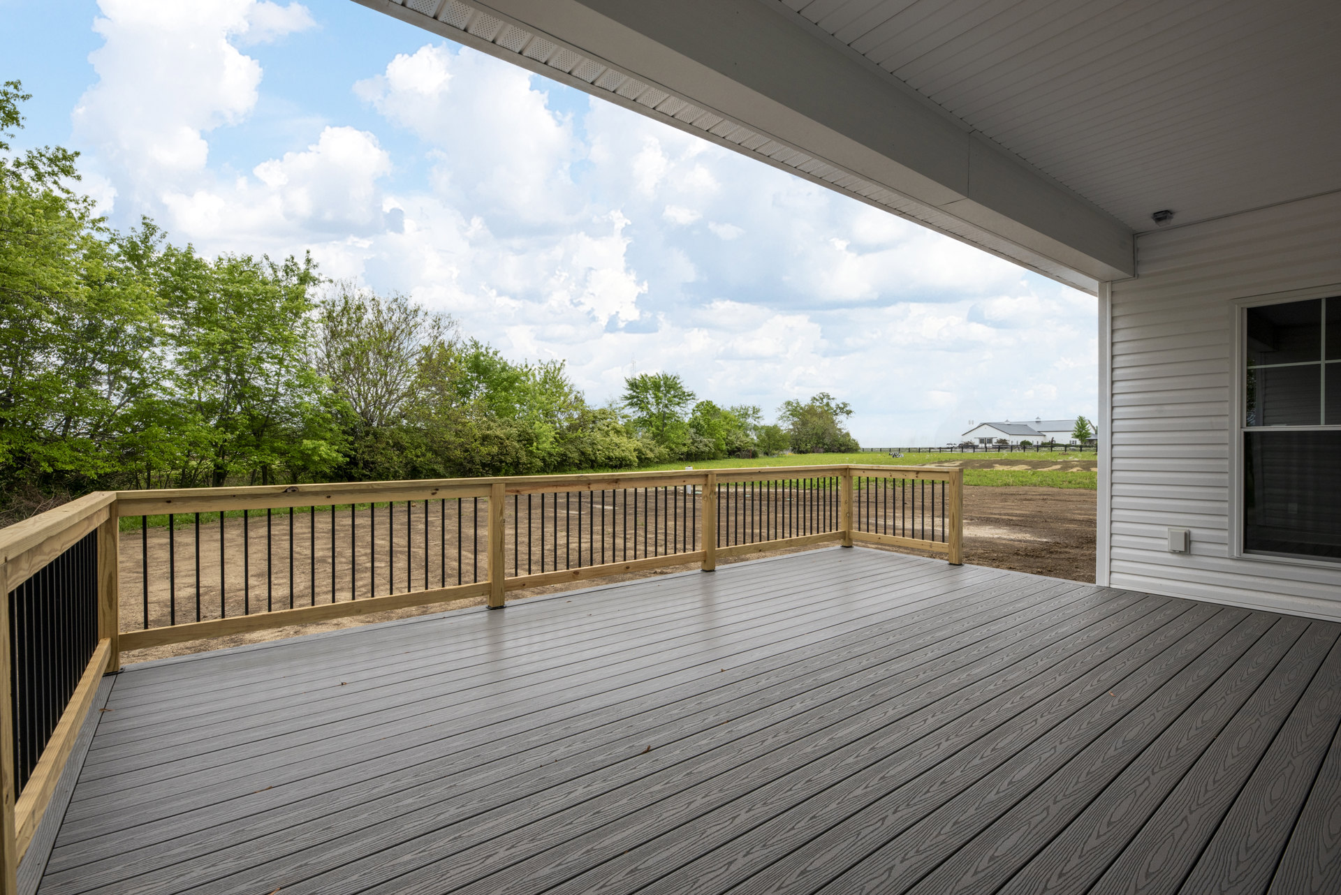 Wooden deck with railing, white-framed window, fenced yard, and trees in the background