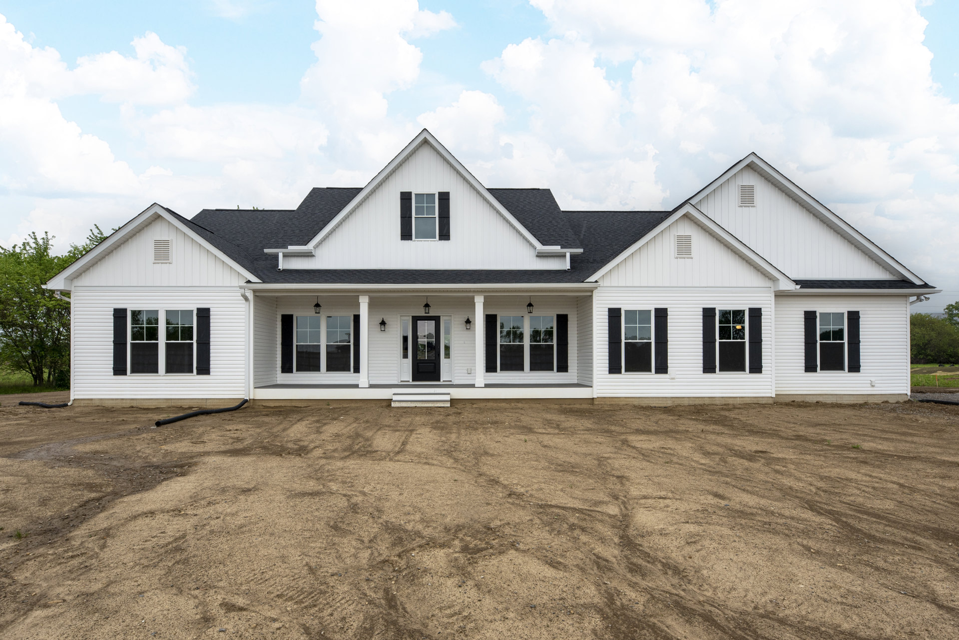 White house with black trim and white-framed windows, dirt driveway in front, blue sky overhead