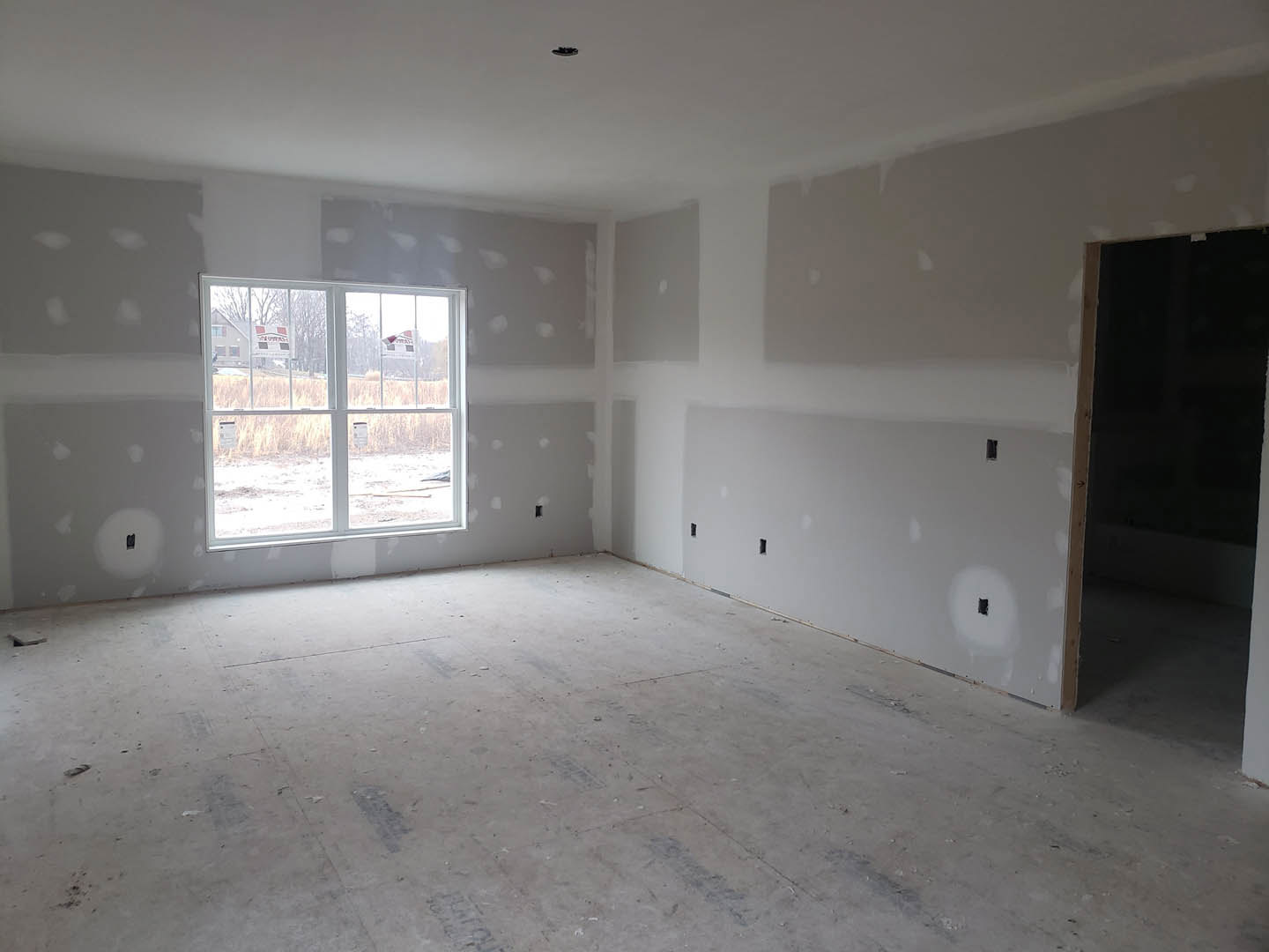 White plaster walls and ceiling, light wood flooring, single window with signage, black square screen mounted on wall, doorway leading to adjacent space
