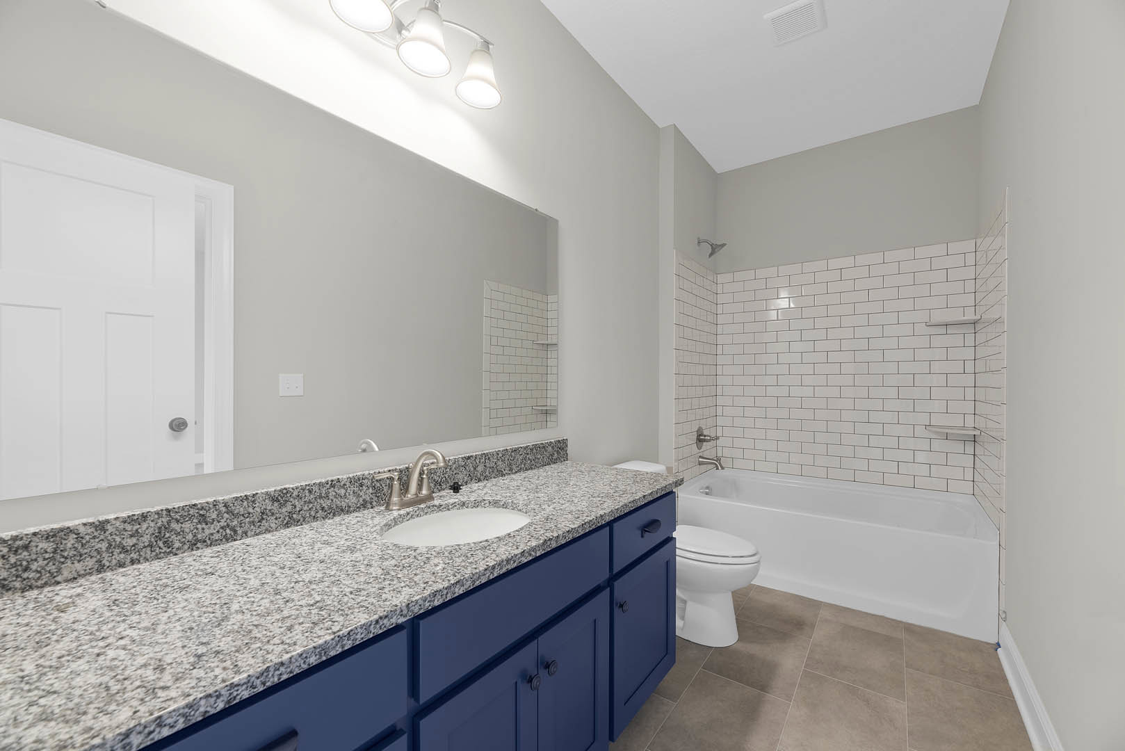 Bathroom with blue cabinets, granite countertop, undermount sink, freestanding tub, white toilet, silver fixtures, and white door with silver doorknob