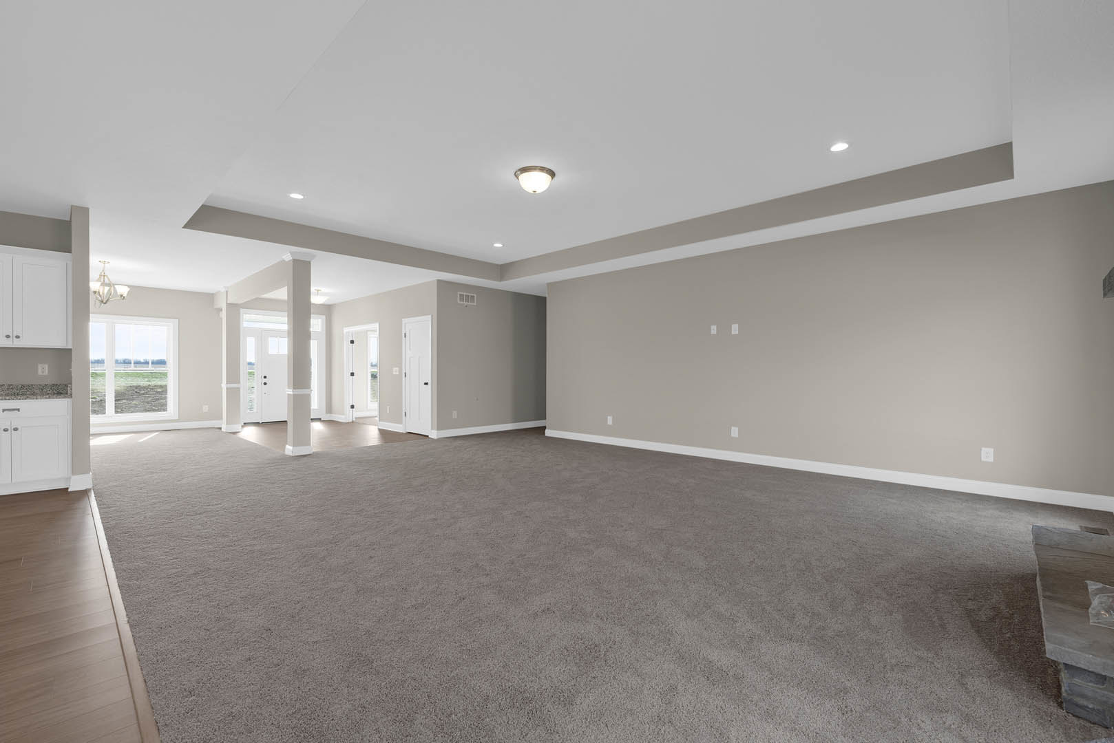 Spacious carpeted room with white ceiling, white walls, three-light ceiling fixture, window overlooking grassy field