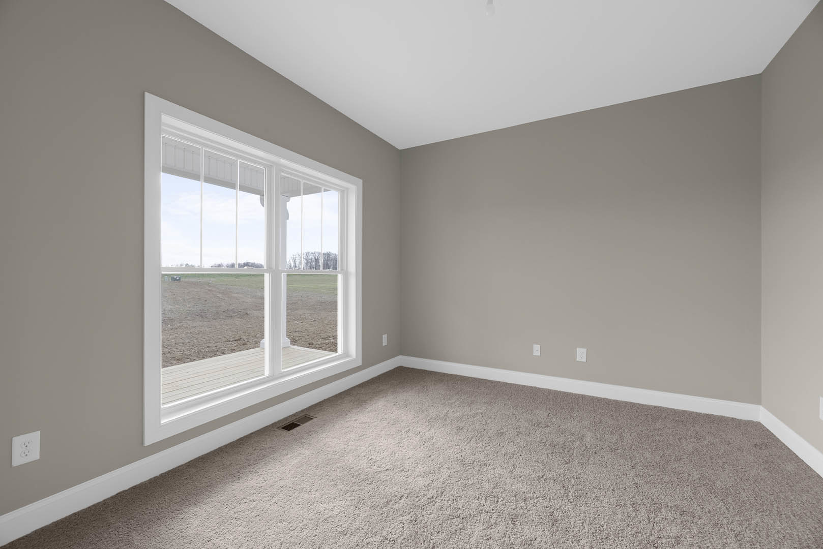 Carpeted room with white walls, large window overlooking grassy field, white electrical outlet, and smooth white ceiling with crown molding
