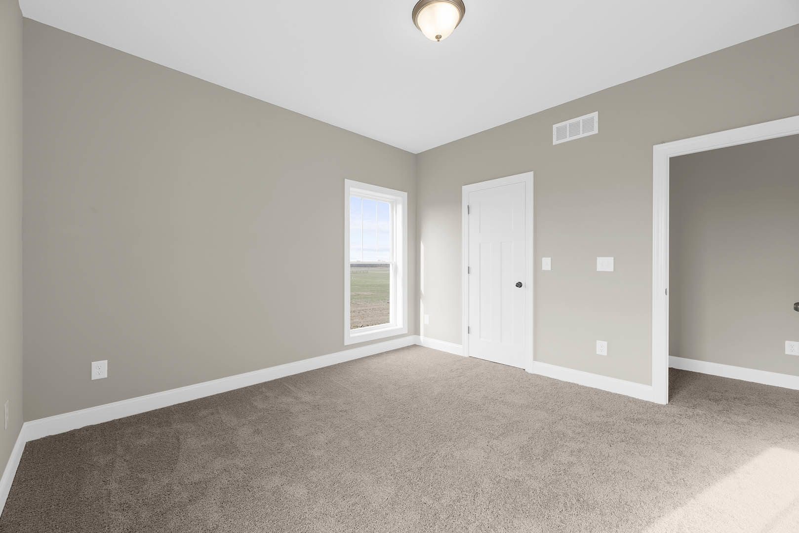 Carpeted room with white walls, white door featuring a black knob, window overlooking a grassy field, ceiling light fixture
