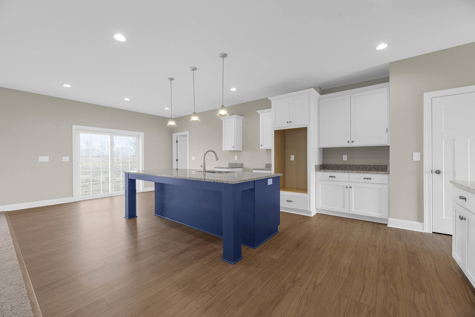 Blue kitchen island with granite countertop, silver curved faucet, wood flooring, glass door behind dining table, white cabinetry and doors
