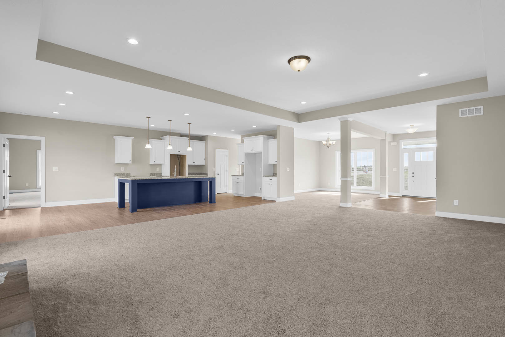Spacious open room featuring a blue kitchen island with wood flooring, carpeted area, white door with black handle, and ceiling-mounted light fixture.
