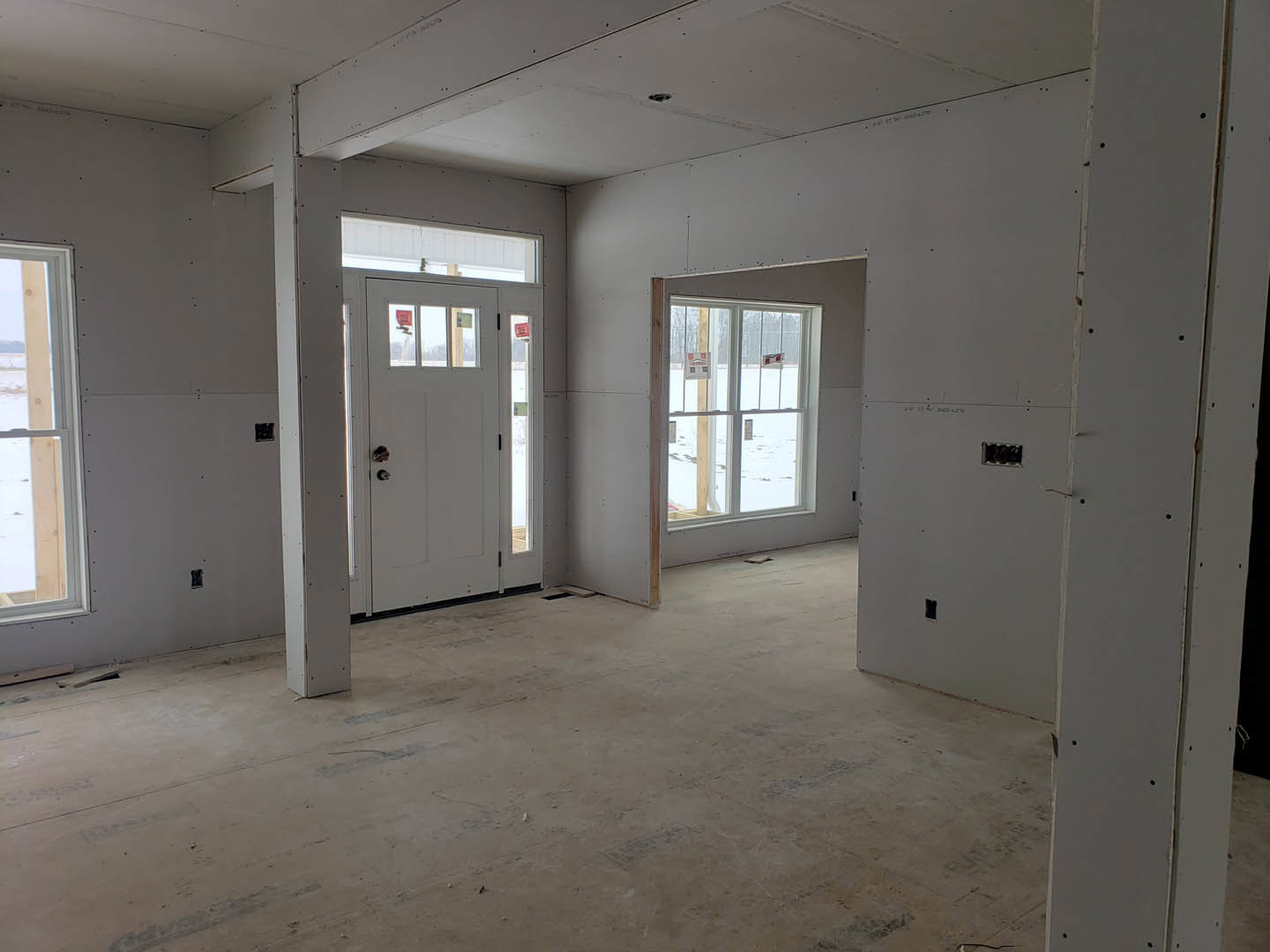 Bright room with white paneled door, adjacent window featuring a wooden beam, plaster walls, and light flooring