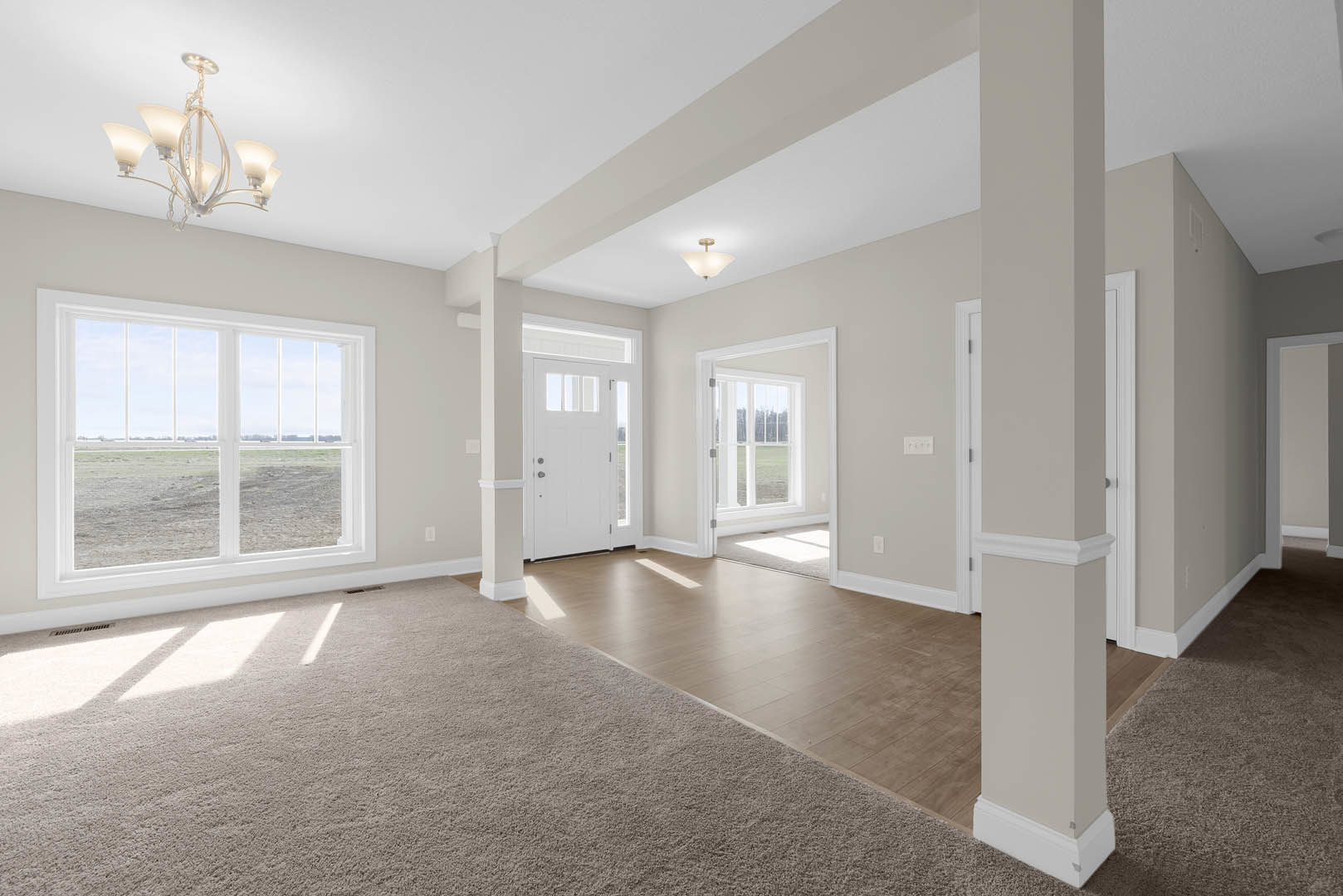 White-walled room featuring a white door with glass panes, a window overlooking a grassy field, five-shade light fixture, white-shaded ceiling light, carpeted area transitioning to