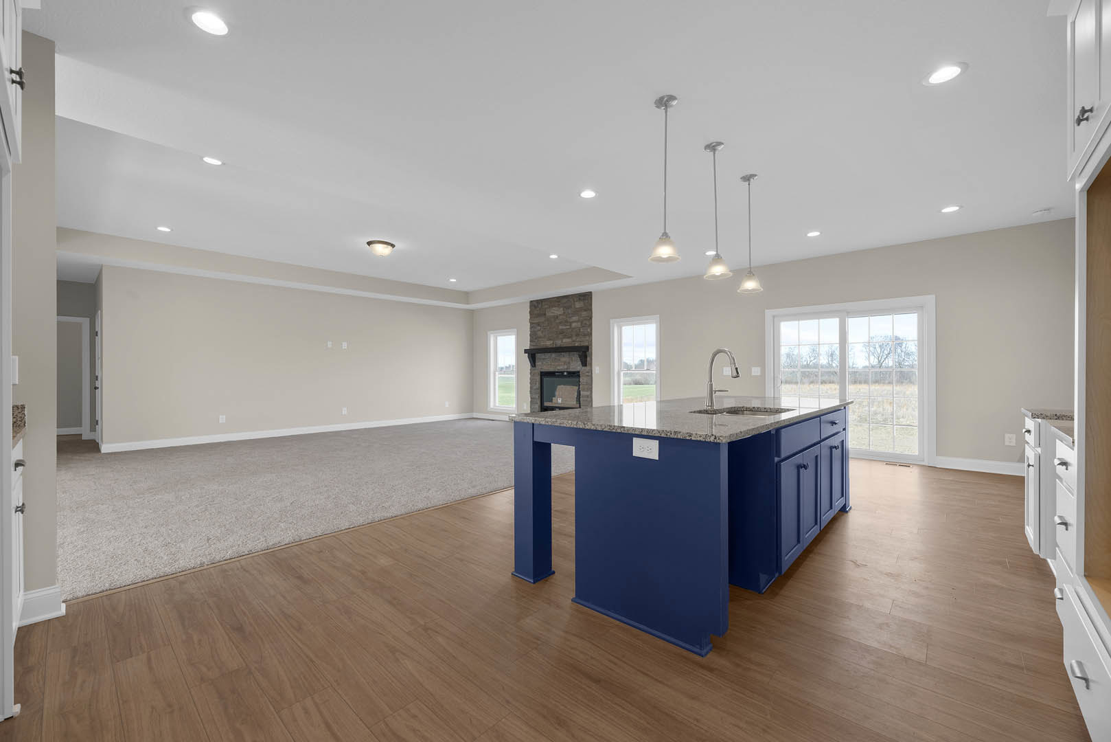 Marble-topped kitchen island with built-in sink and modern faucet, surrounded by cabinetry and large windows, recessed ceiling lights overhead, hardwood flooring throughout