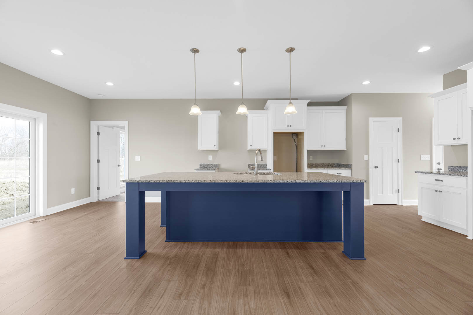 Blue kitchen island with white countertop, wood flooring, white cabinetry, black and metal door handles, window overlooking snowy field, blue accent wall