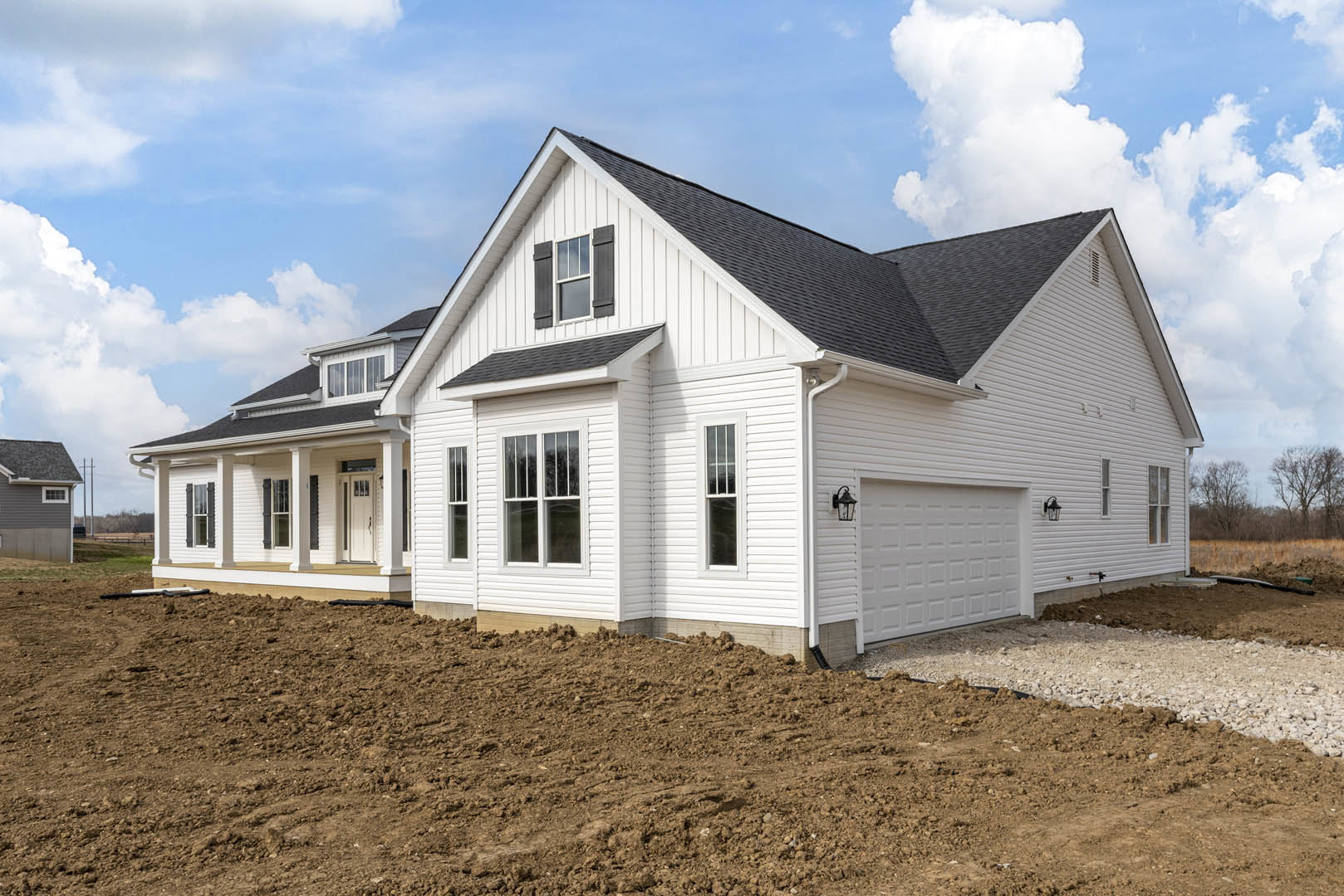 Two-story house under construction with white-framed windows, attached garage, dirt pile in front yard, and blue sky overhead