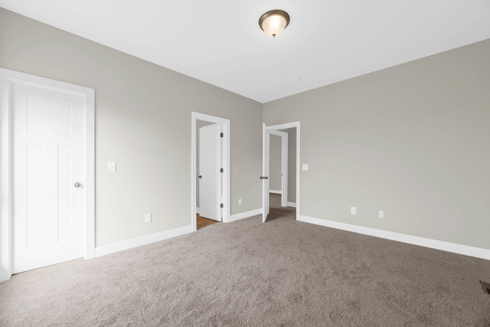 Carpeted room with white walls, white ceiling, modern light fixture, white door with silver handle, second white door with black knobs, and white trim