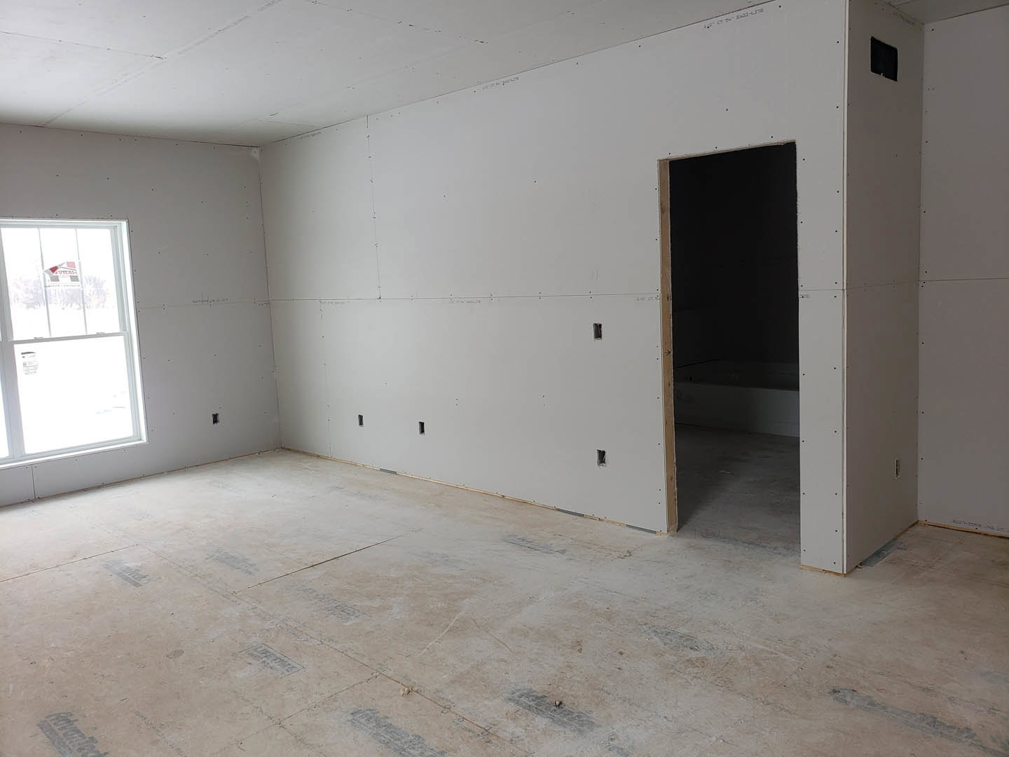 White-walled room with concrete floor, single window featuring a sign, wooden-framed blackboard, white ceiling marked with black streaks, and a closed door