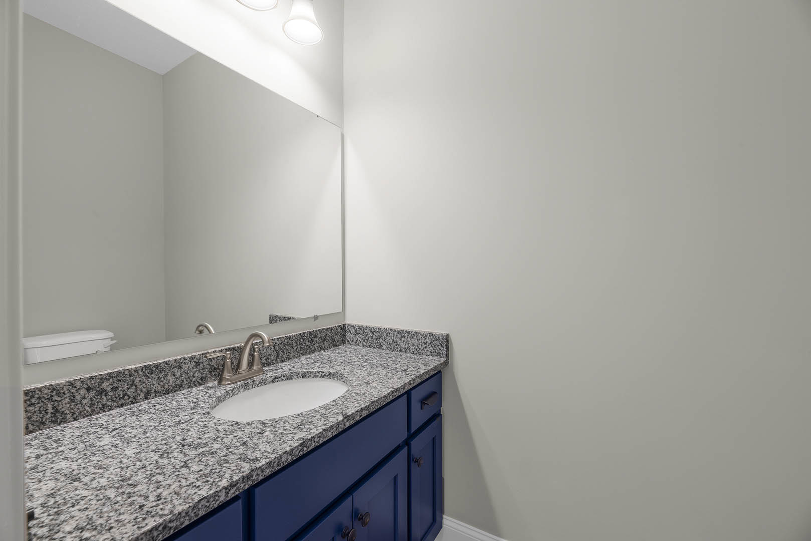 Marble countertop with undermount sink, chrome faucet, large framed mirror, white cabinetry, and light tile backsplash in a modern bathroom.