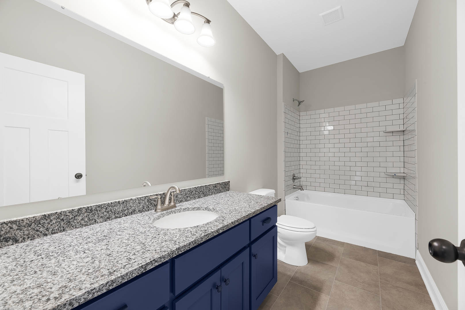 Bathroom with blue vanity cabinets, white square-paneled door, modern light fixture, white toilet, and rectangular sink on stone countertop