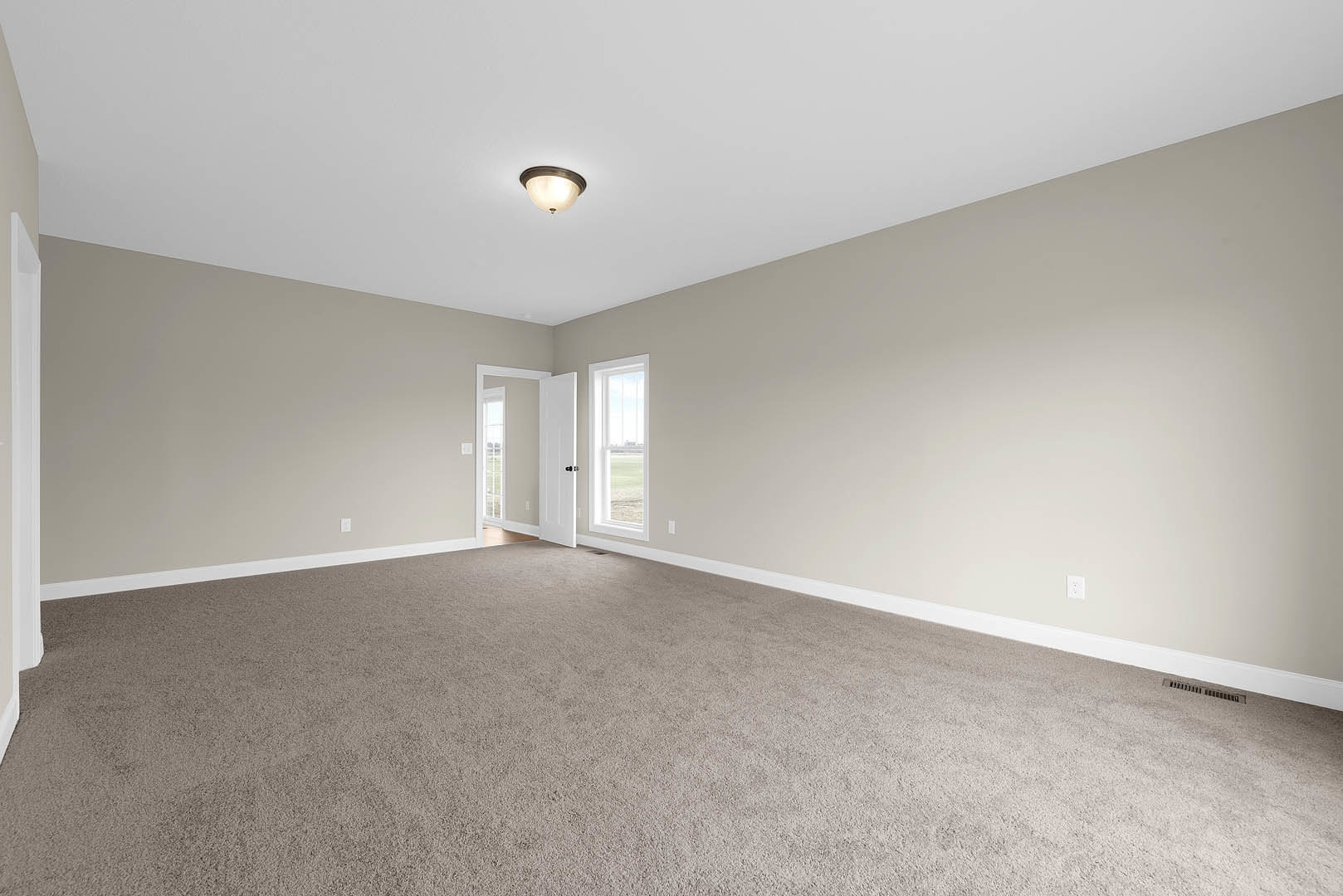 Carpeted room with white door, ceiling light fixture, and window overlooking grassy field