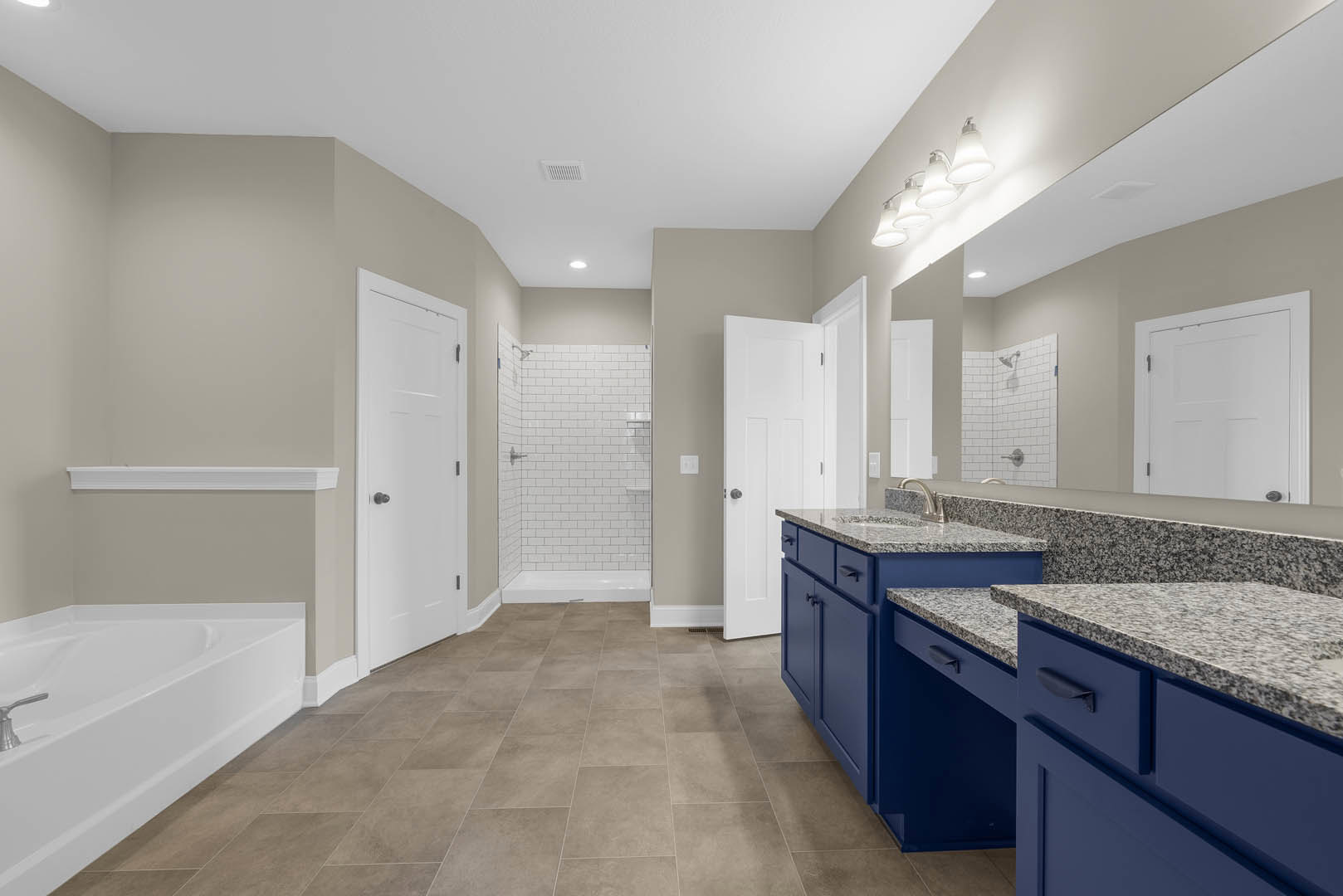 Bathroom featuring marble flooring, blue cabinetry, white tile shower with built-in shelf, white bathtub with silver faucet, and white door with chrome hardware