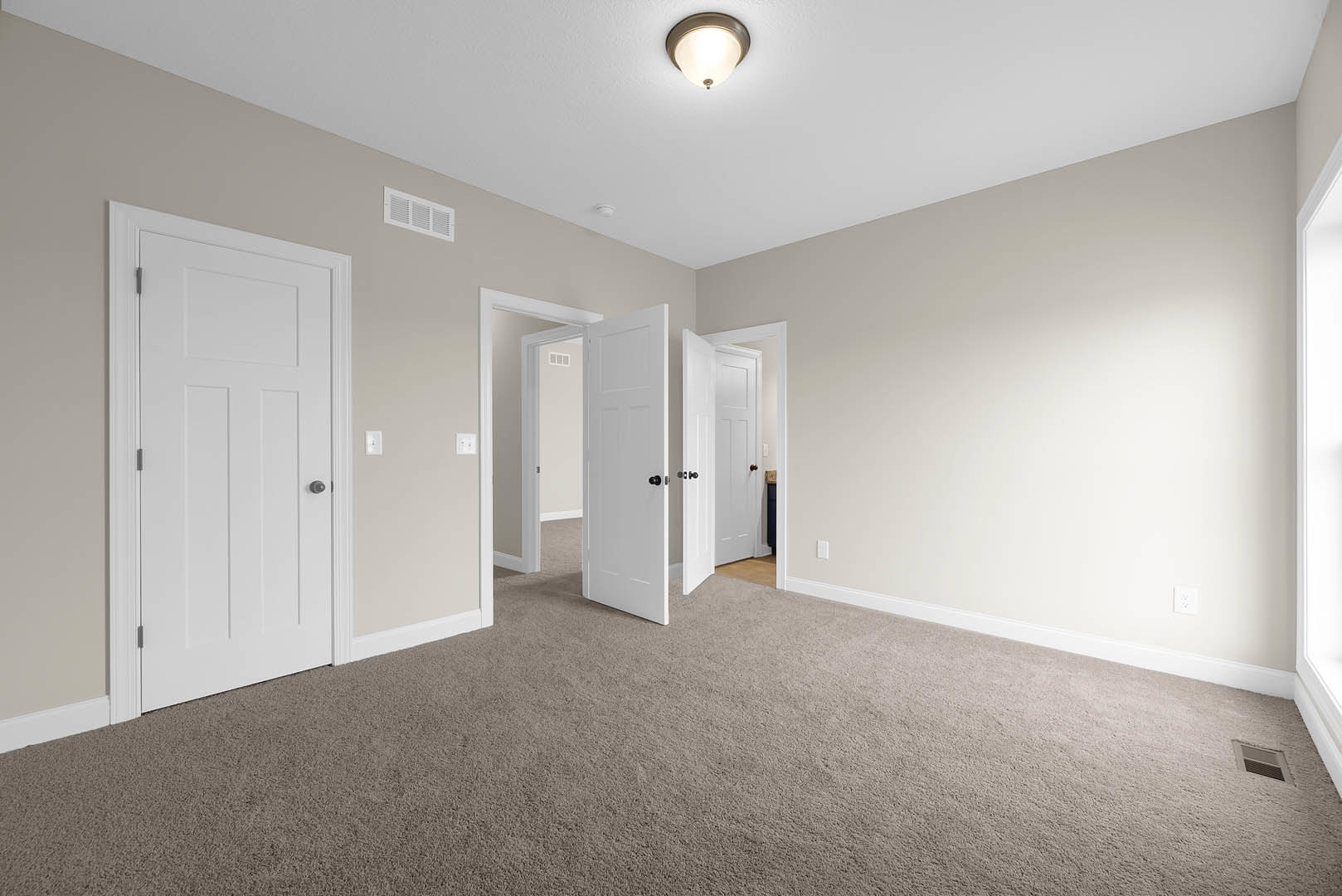 Carpeted room with white paneled doors featuring black knobs, white walls, ceiling light fixture, wall vent, and crown molding