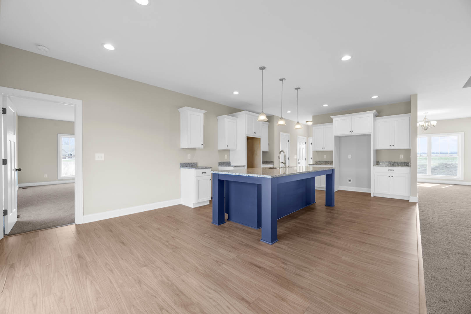 Blue kitchen island with marble countertop, wood flooring, white cabinetry with black countertop, open door, window overlooking ocean