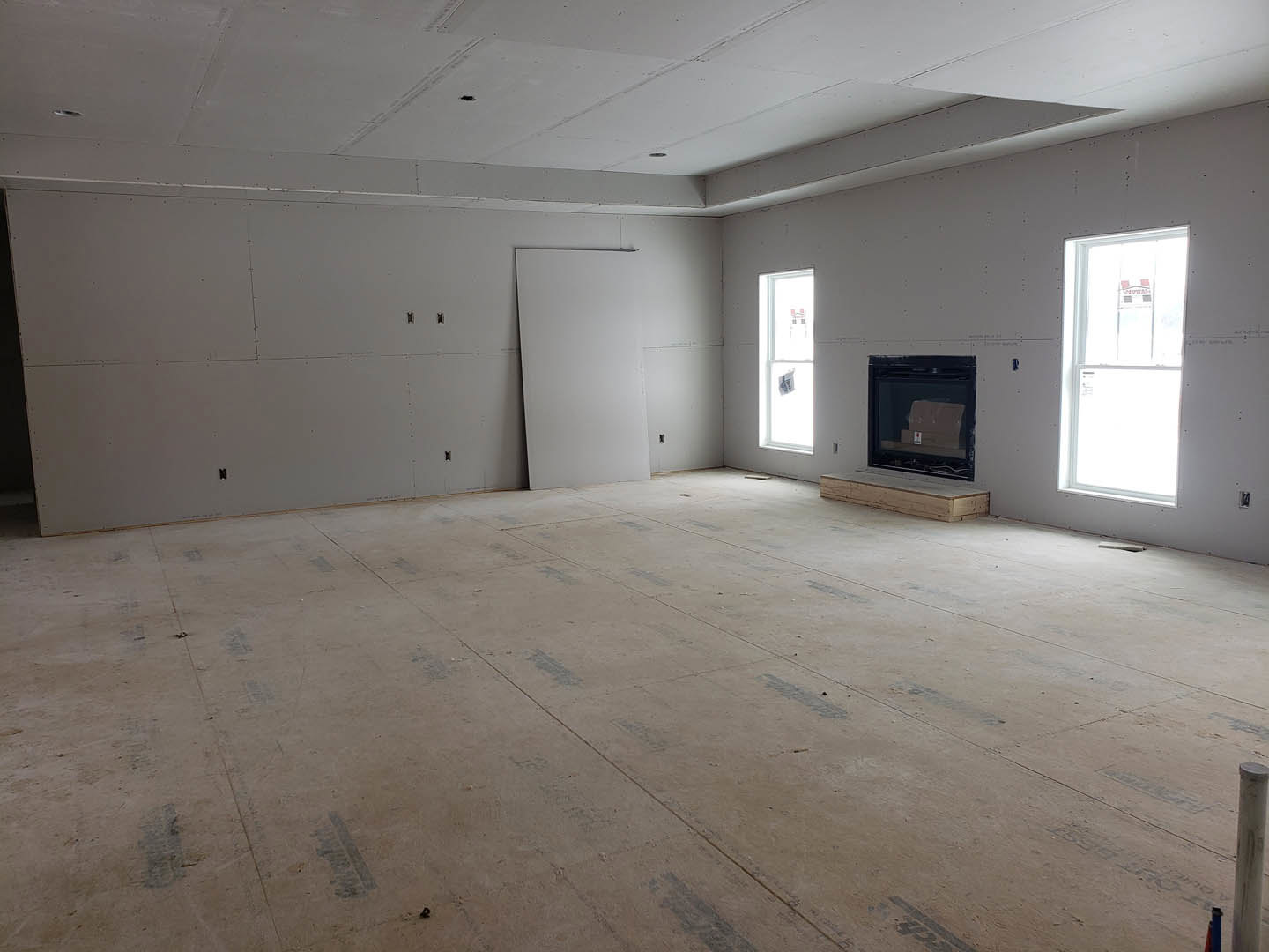 Living room with white plaster walls, black trim, tile flooring, large windows, and a central fireplace; wooden surface and glass door visible.