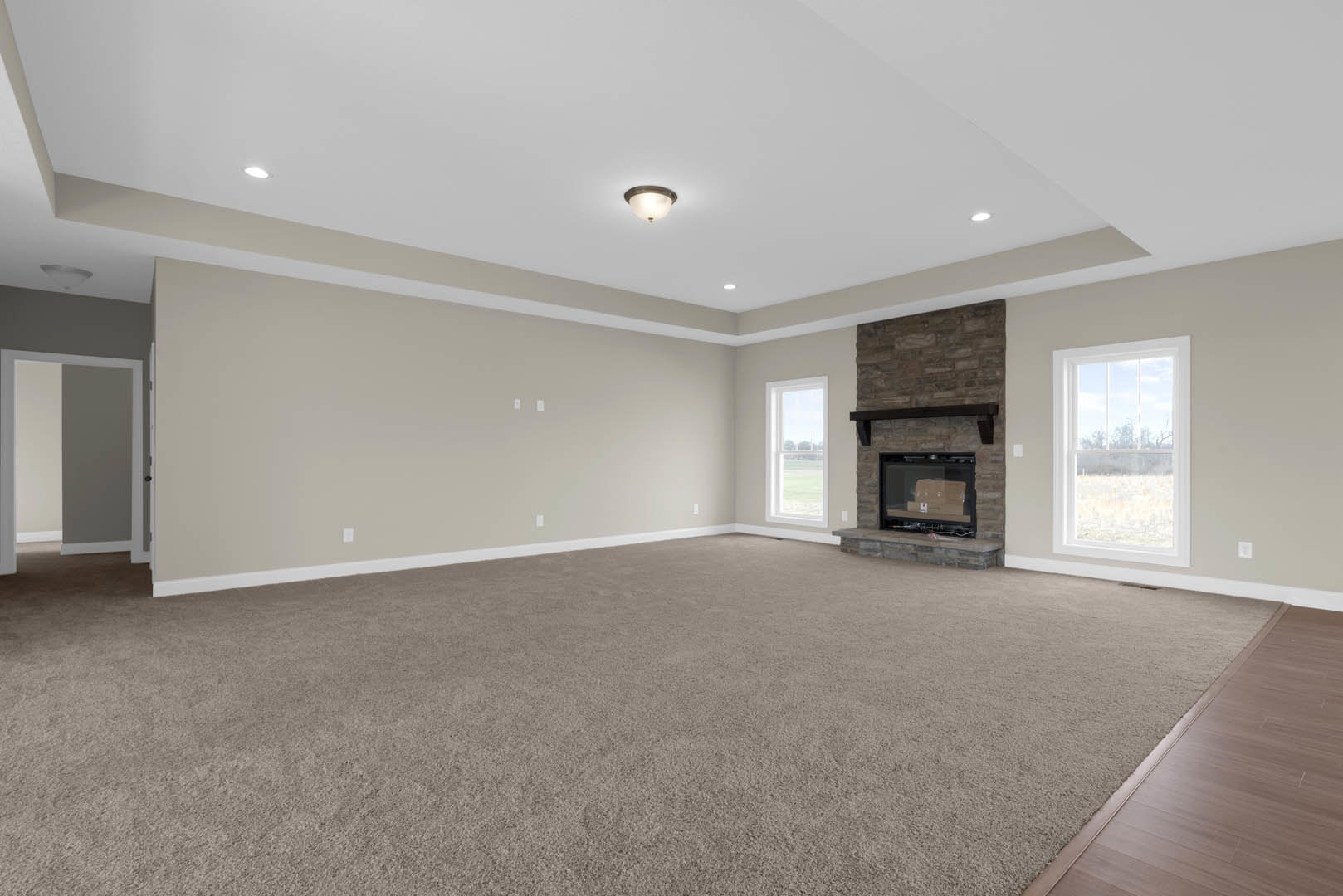Spacious empty room with carpeted floor, central fireplace, large window overlooking a field, ceiling light fixture illuminated, white plaster walls, decorative molding, and glass