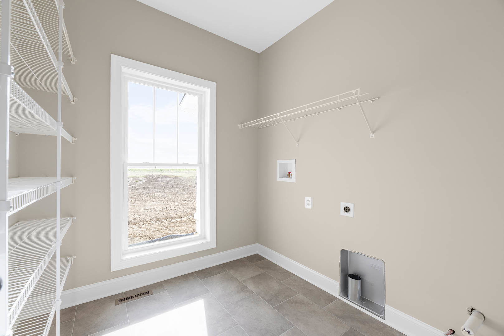 White plaster walls and ceiling, built-in white shelf, large window overlooking dirt field, silver trash can with black lid recessed into wall, light wood floor