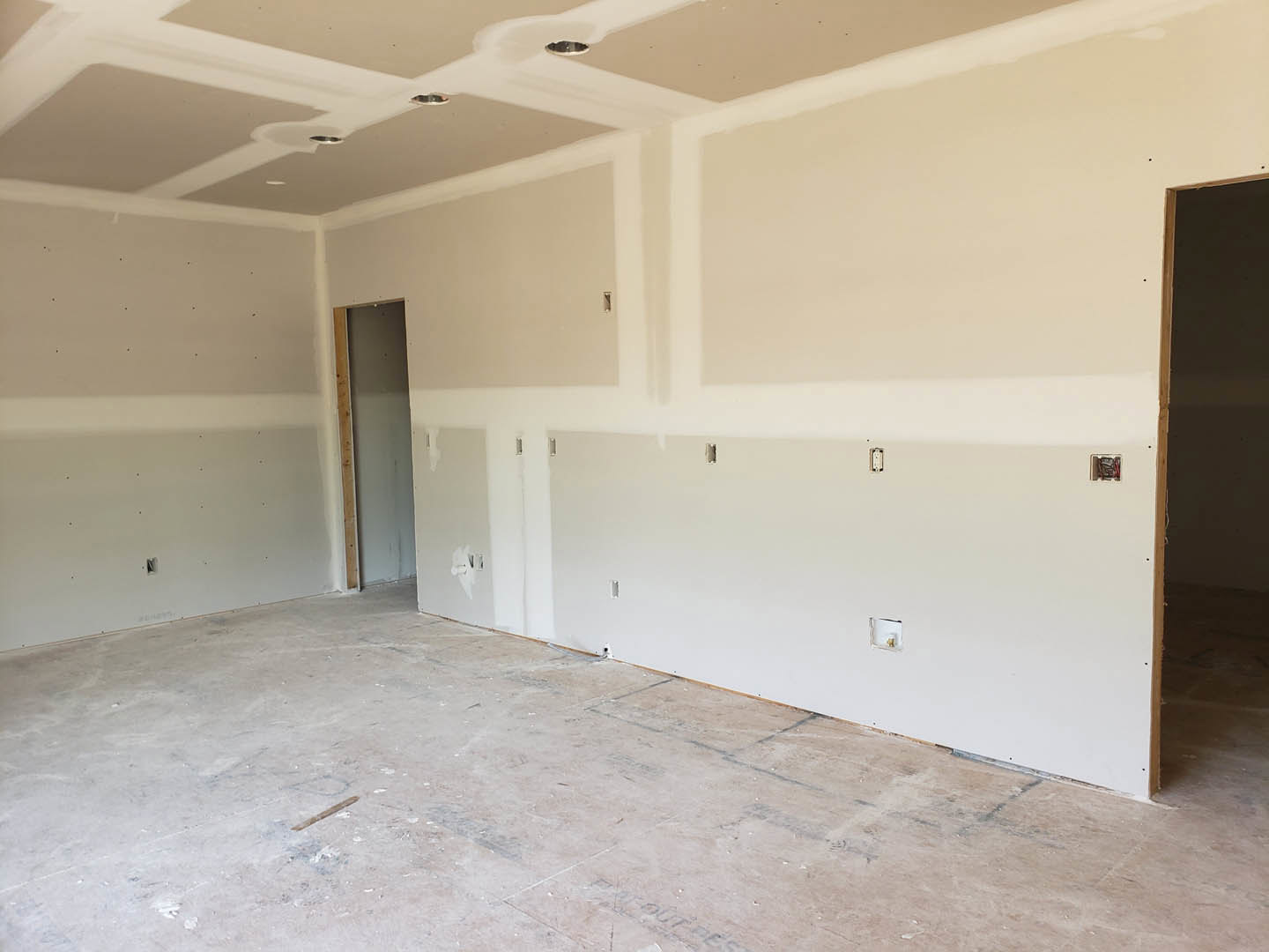 White walls with visible holes, wooden door frame, light-colored flooring featuring black lines, ceiling with recessed opening.