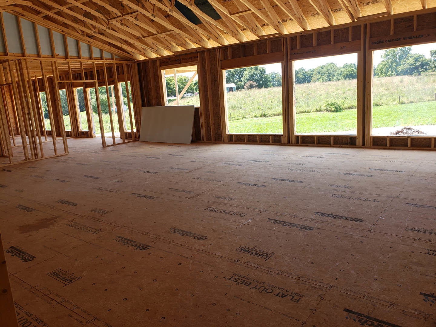 Living room with exposed wood ceiling beams, large windows, light-colored walls, and hardwood flooring