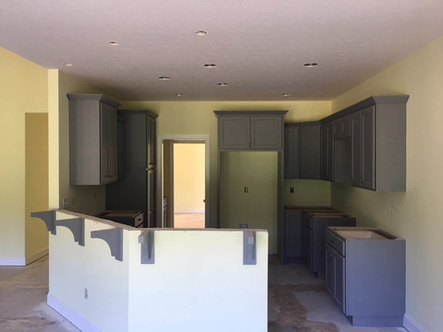Modern kitchen featuring grey shaker cabinets, white walls with gray brackets, stainless steel appliances, light wood flooring, and recessed ceiling lighting.
