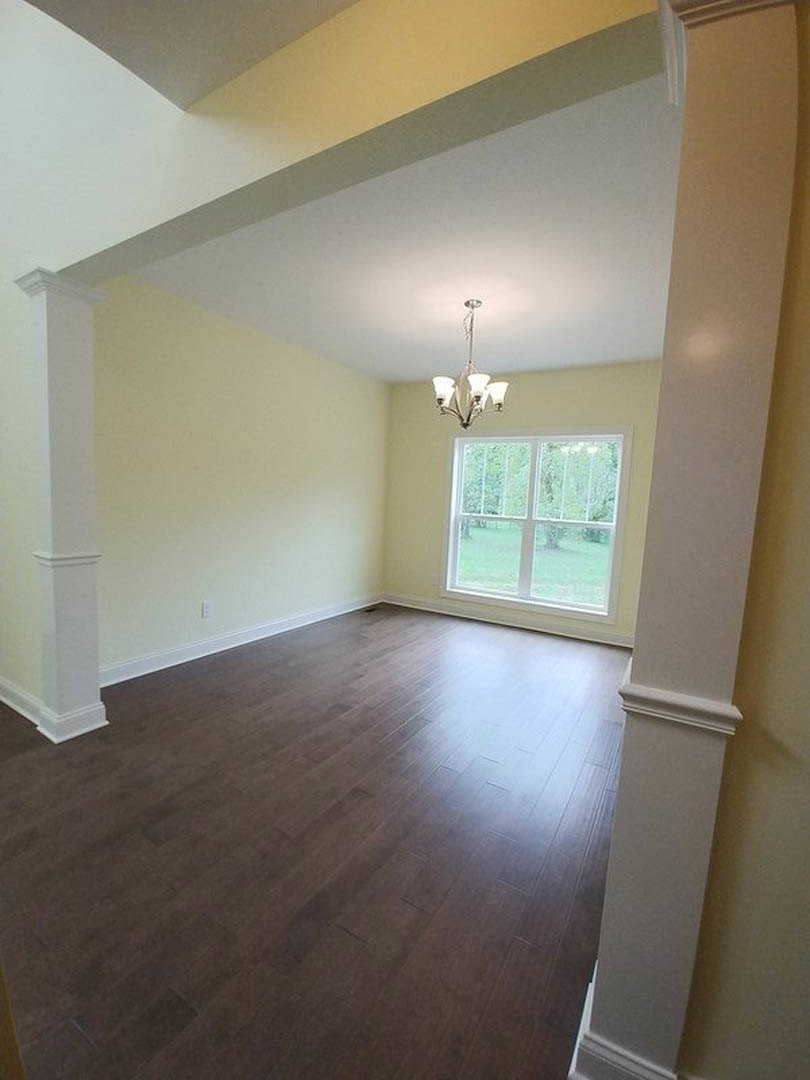 Room with dark hardwood flooring, white plaster walls, ceiling-mounted light fixture, and window offering outdoor view
