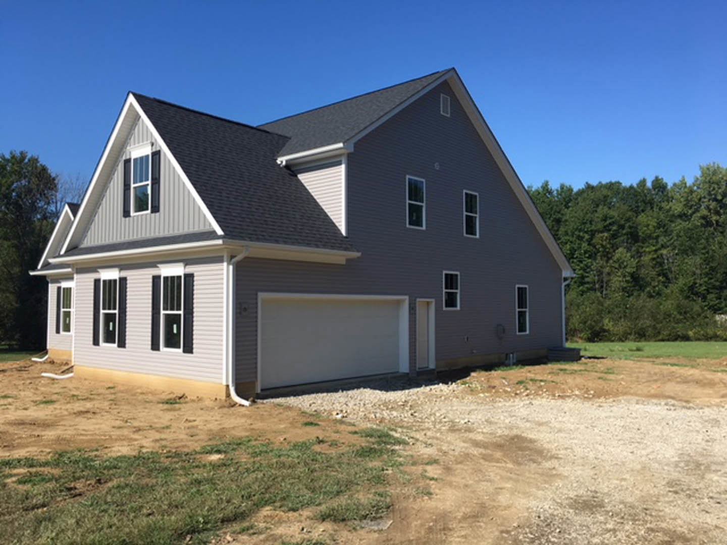 Two-story home with white siding, attached garage, paved driveway, large windows with white frames, mature trees in the background