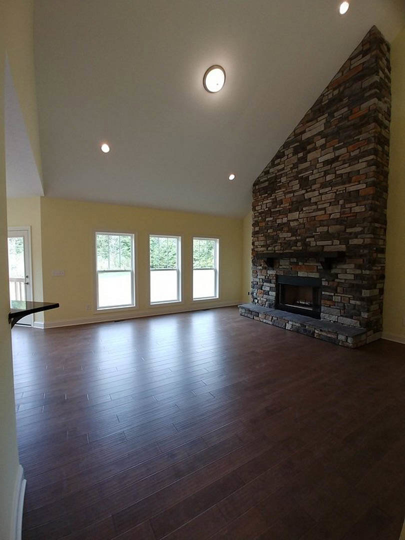 Living room with hardwood floors, stone fireplace, large window framing outdoor trees, neutral walls, and white ceiling