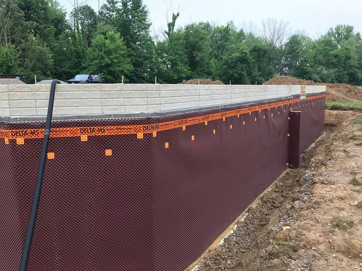 White block wall with brown metal fence, green trees and grass in the background, outdoor residential setting.
