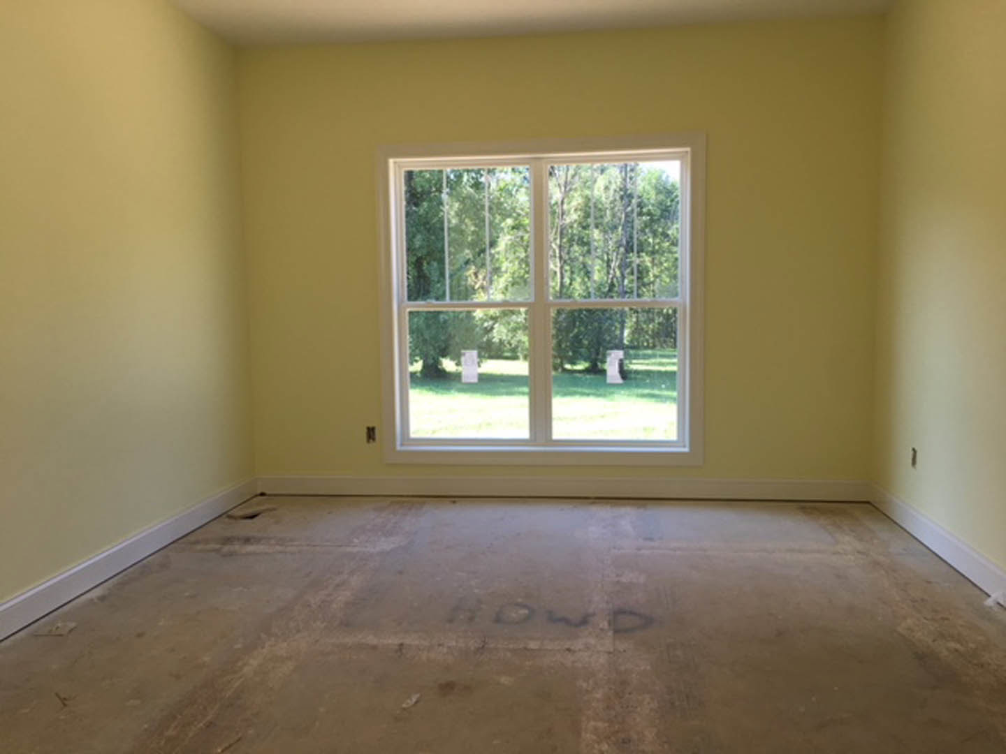 Sunlit room featuring a large window overlooking trees, smooth concrete flooring, white plaster walls, and minimalist interior finishes