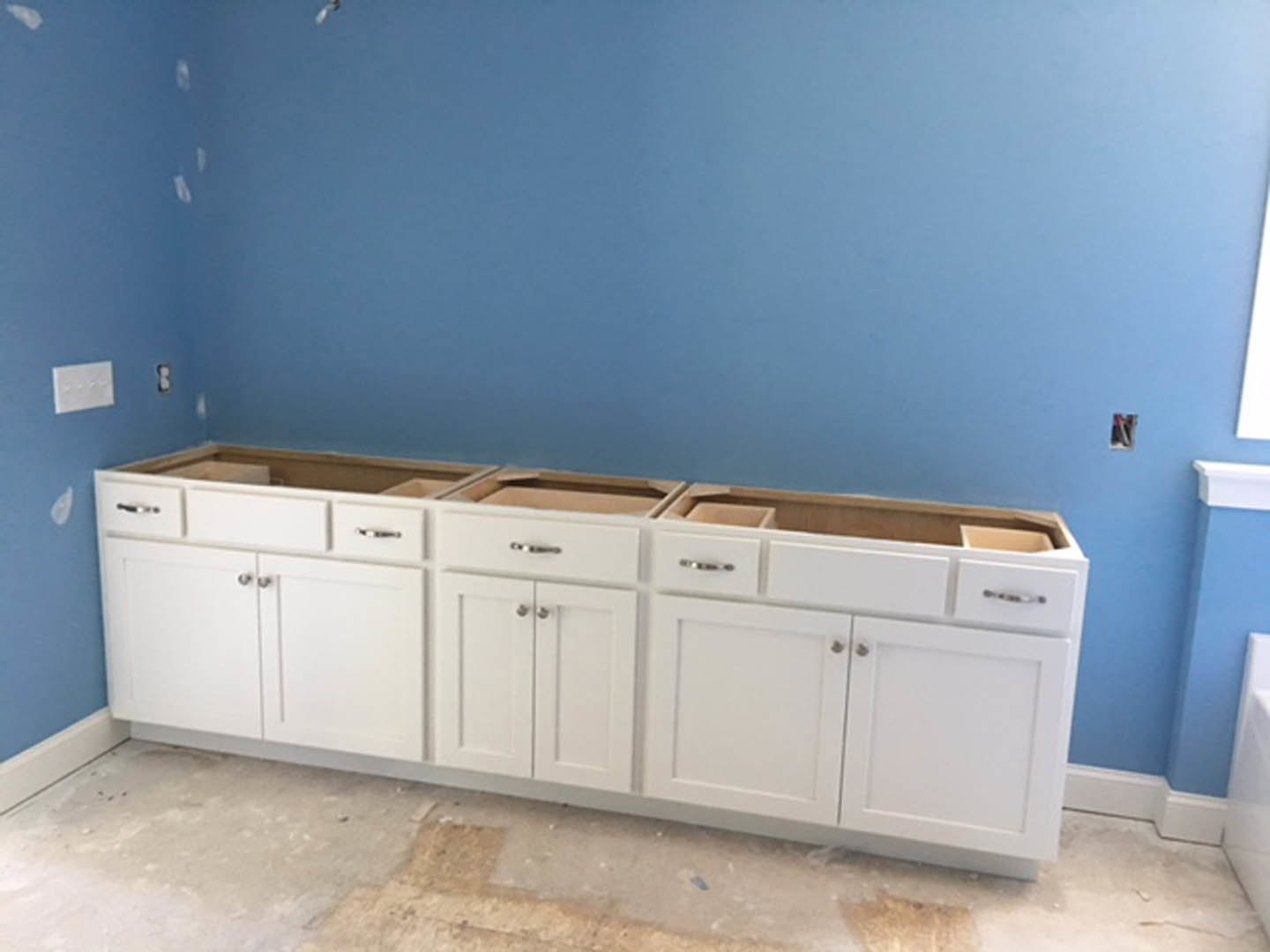 White shaker-style kitchen cabinets with brushed metal knobs, blue accent wall, quartz countertop, stainless steel sink, and wood flooring