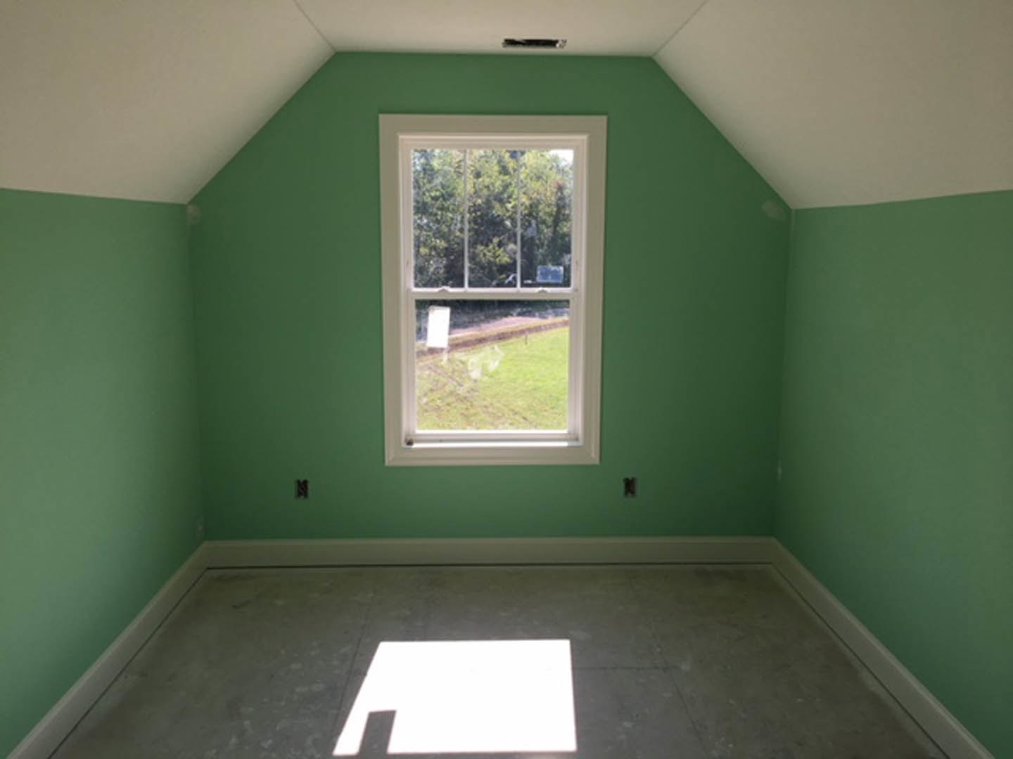 Green-painted walls and white tile floor in a room with a large window overlooking a grassy field and trees; sunlight casts shadows across the floor.