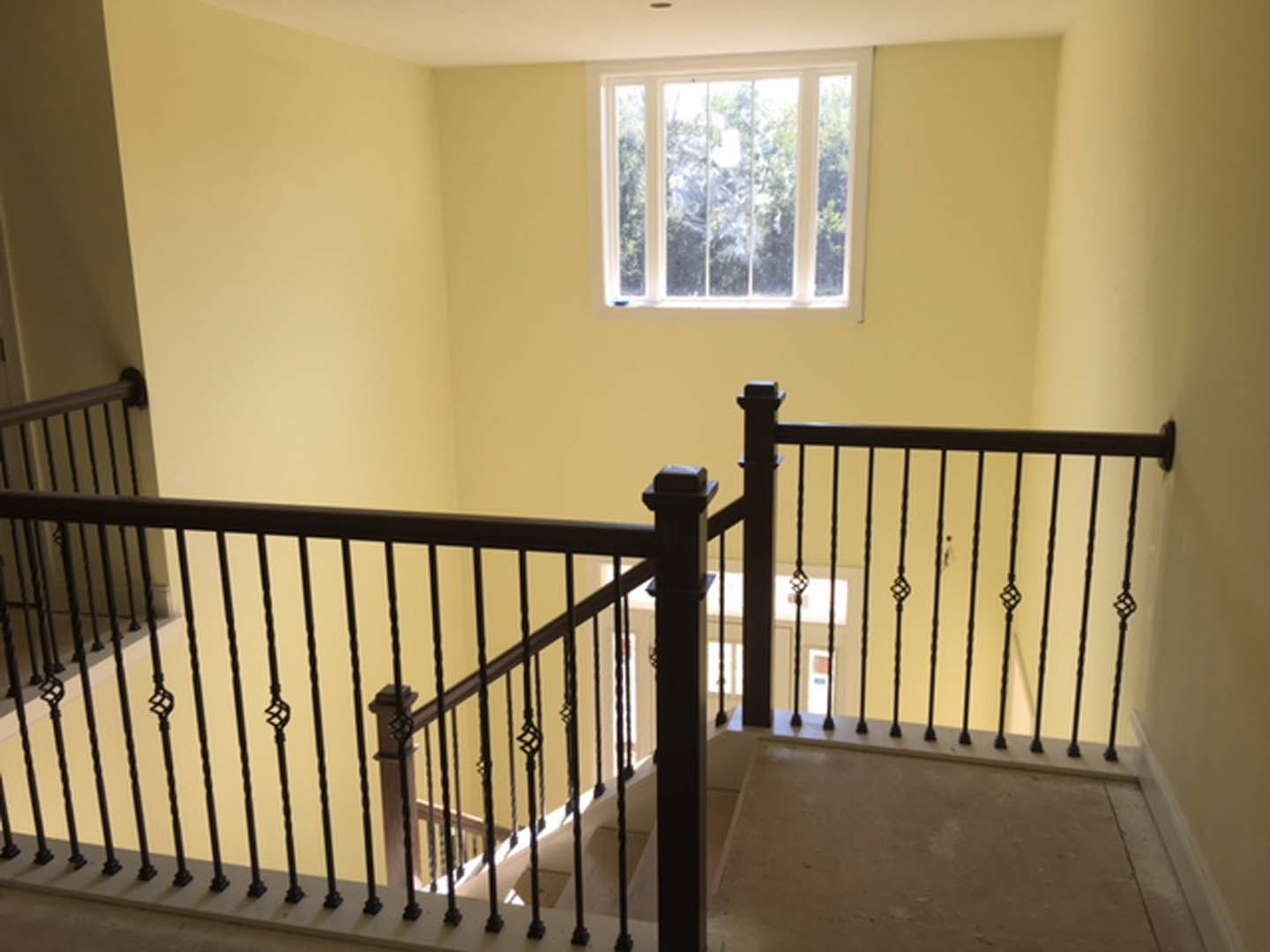 Wood staircase with black iron railing in a bright room, large window revealing leafy trees outside