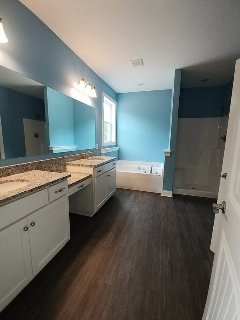 Bathroom with blue accent wall, white cabinetry, granite countertop, window letting in natural light, bathtub with chrome faucets, tile flooring, and modern fixtures.