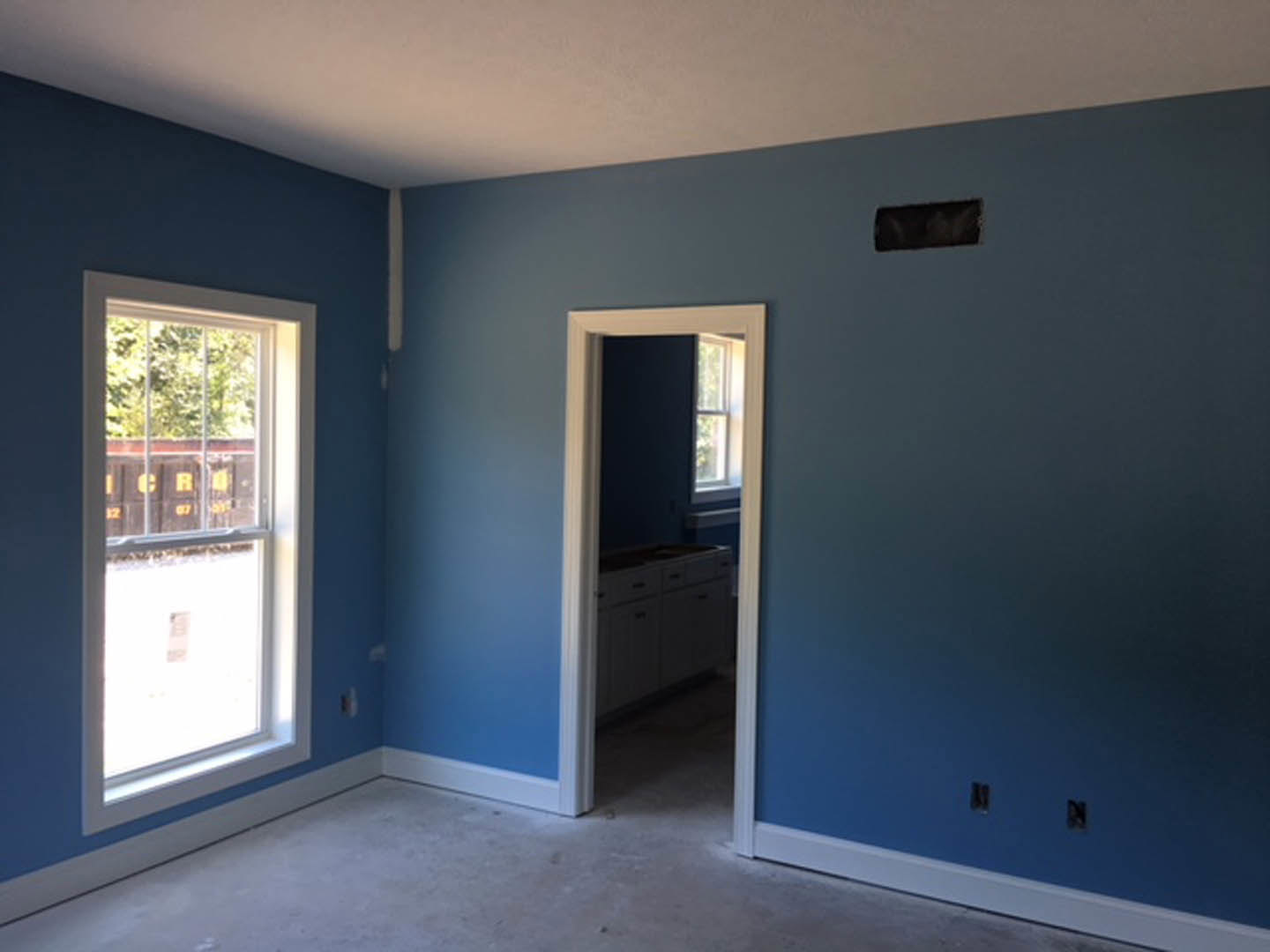 Blue-painted walls, white-framed window, white cabinet with drawers, kitchen sink beneath window, door, light-colored flooring, close-up of white object on floor, black object with