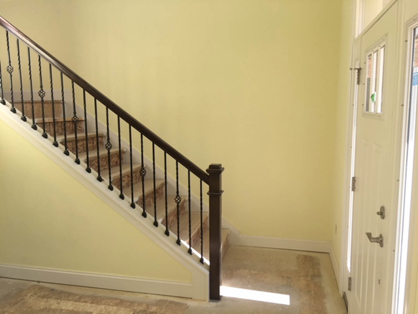 Staircase with matte black metal railing, light plaster walls, concrete floor, white door with sign, modern interior finishes