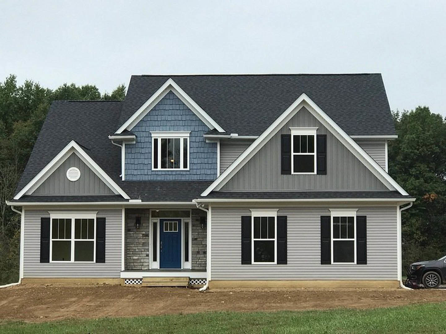 Blue front door with white trim on gray siding, adjacent windows, small porch, and partial view of black car parked in driveway