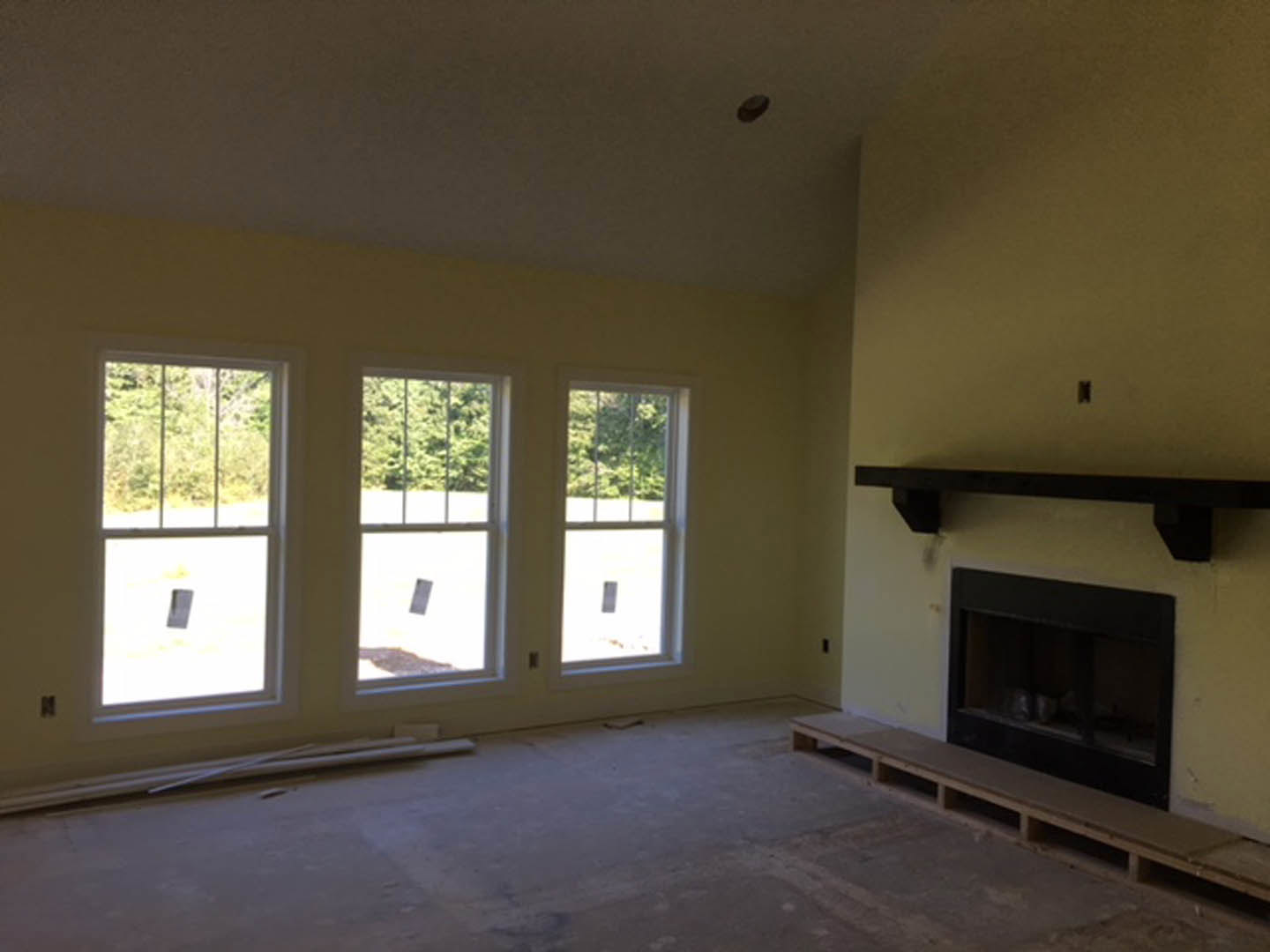 Living room with plaster walls, large windows overlooking trees, glass-door fireplace, wooden bench made from pallets, hardwood flooring